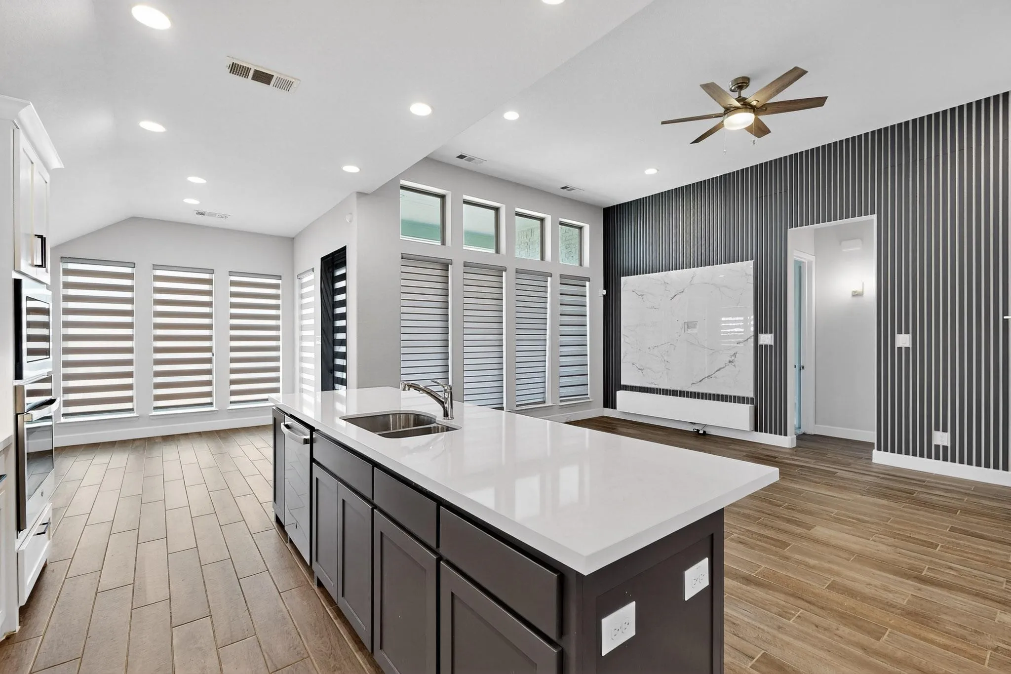 Kitchen featuring an island with sink, light stone counters, wood tiled floors, recessed lighting, and ceiling fan