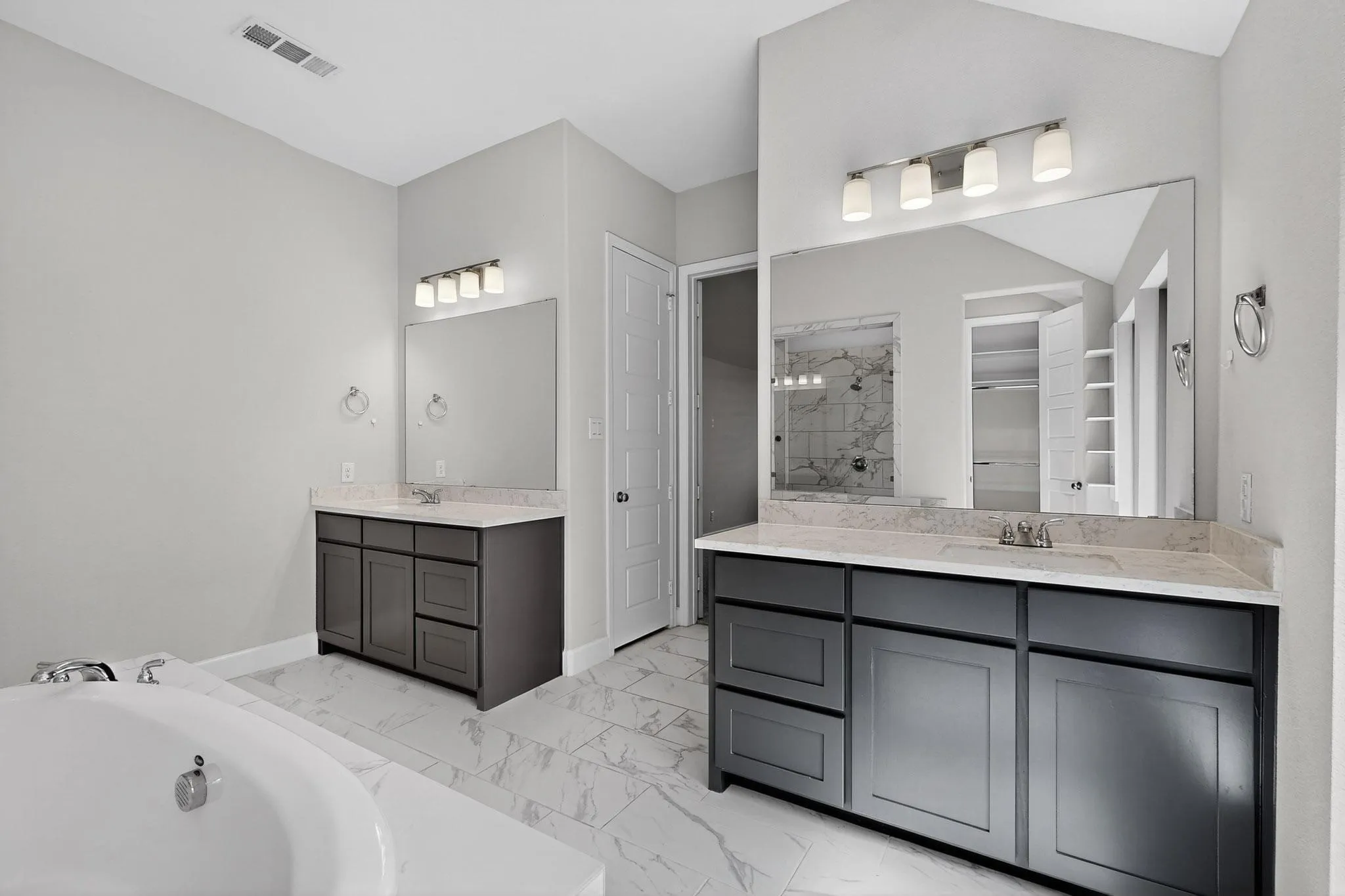 Full bathroom with two vanities, a bath, a stall shower, light marble finish floors, and a walk in closet