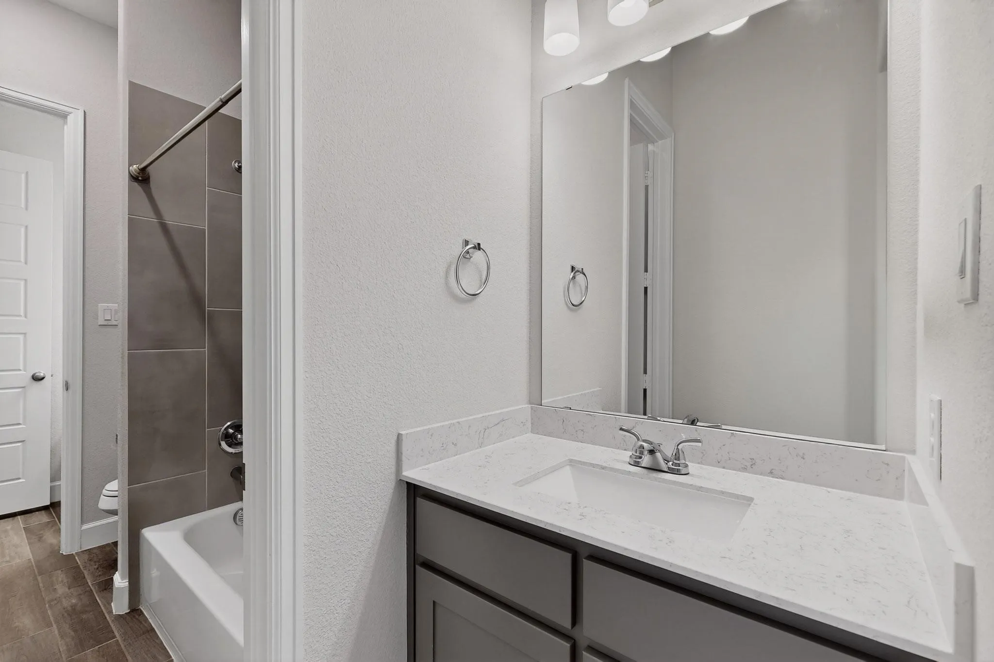 Full bath featuring vanity, washtub / shower combination, a textured wall, and wood finish floors