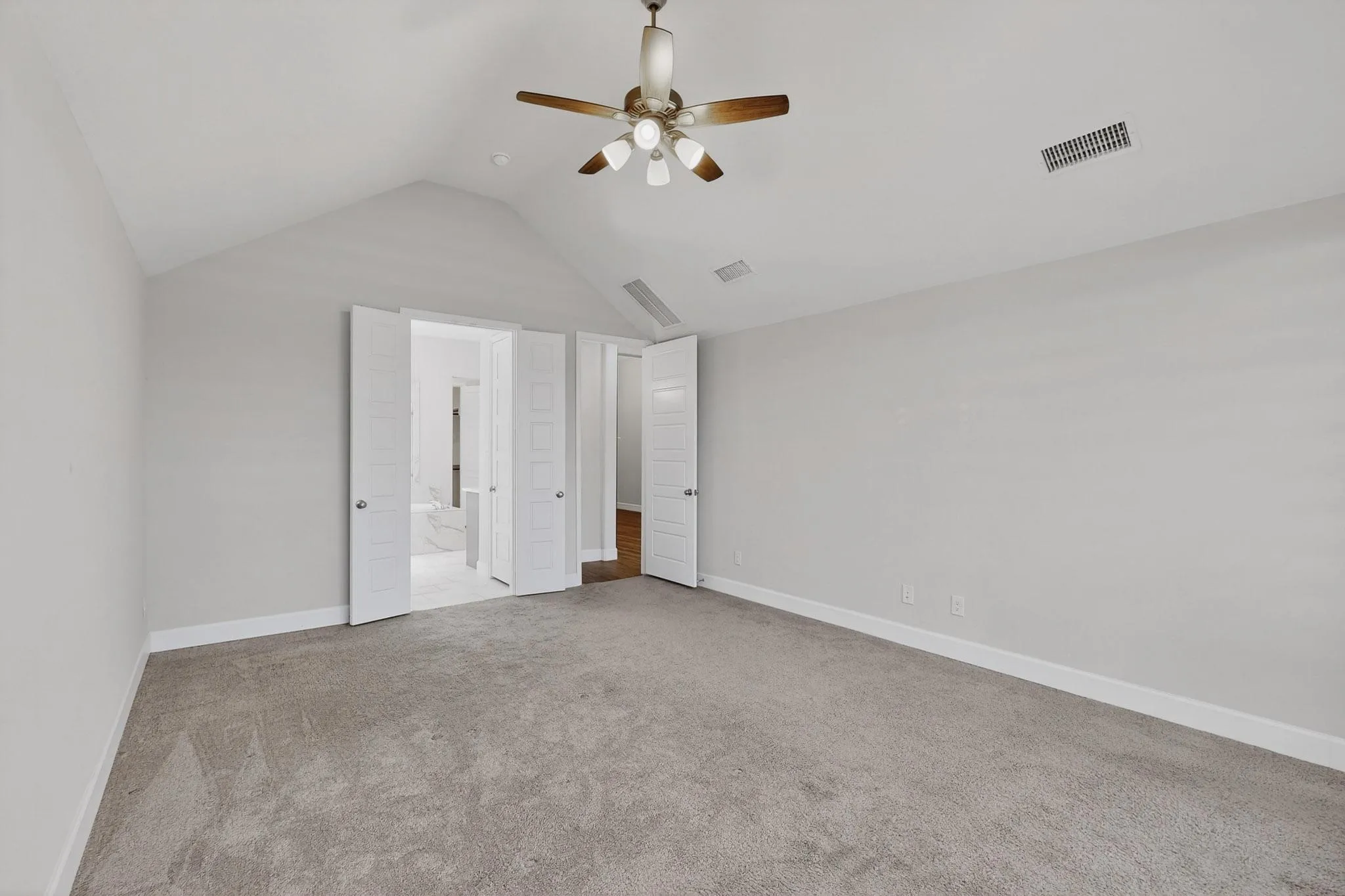 Unfurnished bedroom with light carpet, vaulted ceiling, ceiling fan, and connected bathroom