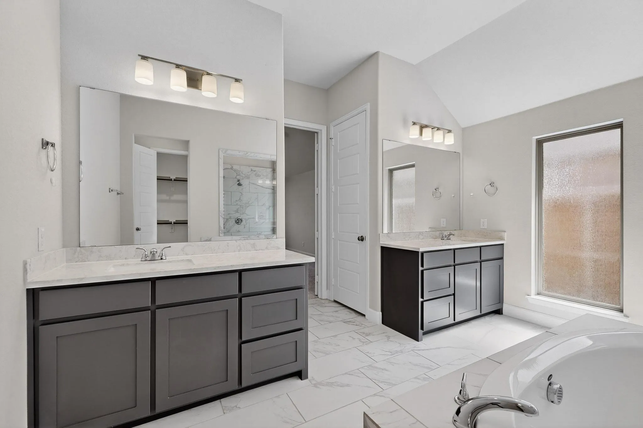 Bathroom featuring two vanities, light marble finish floors, a stall shower, a garden tub, and lofted ceiling