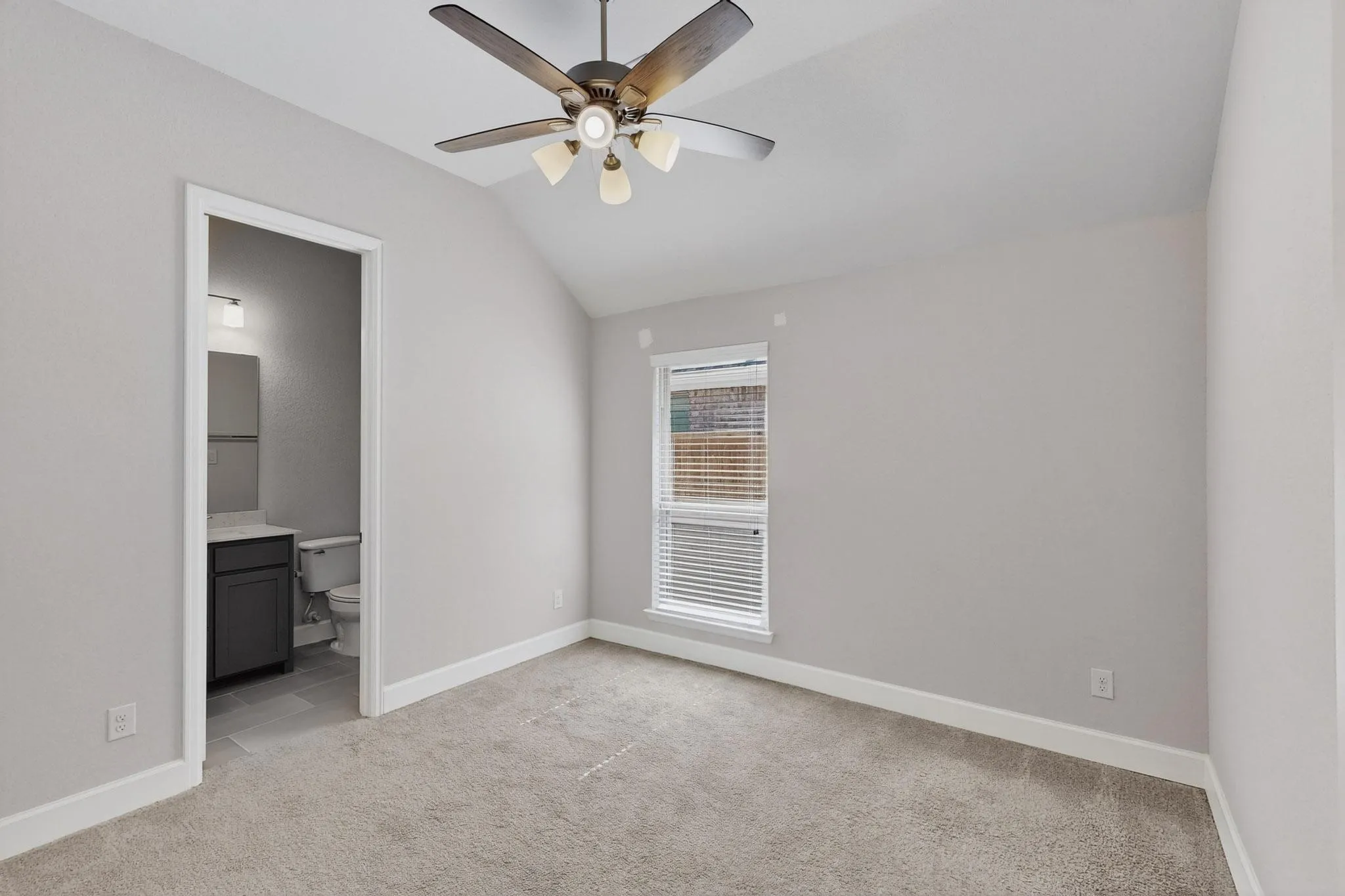 Unfurnished bedroom with vaulted ceiling, light carpet, ceiling fan, and ensuite bath