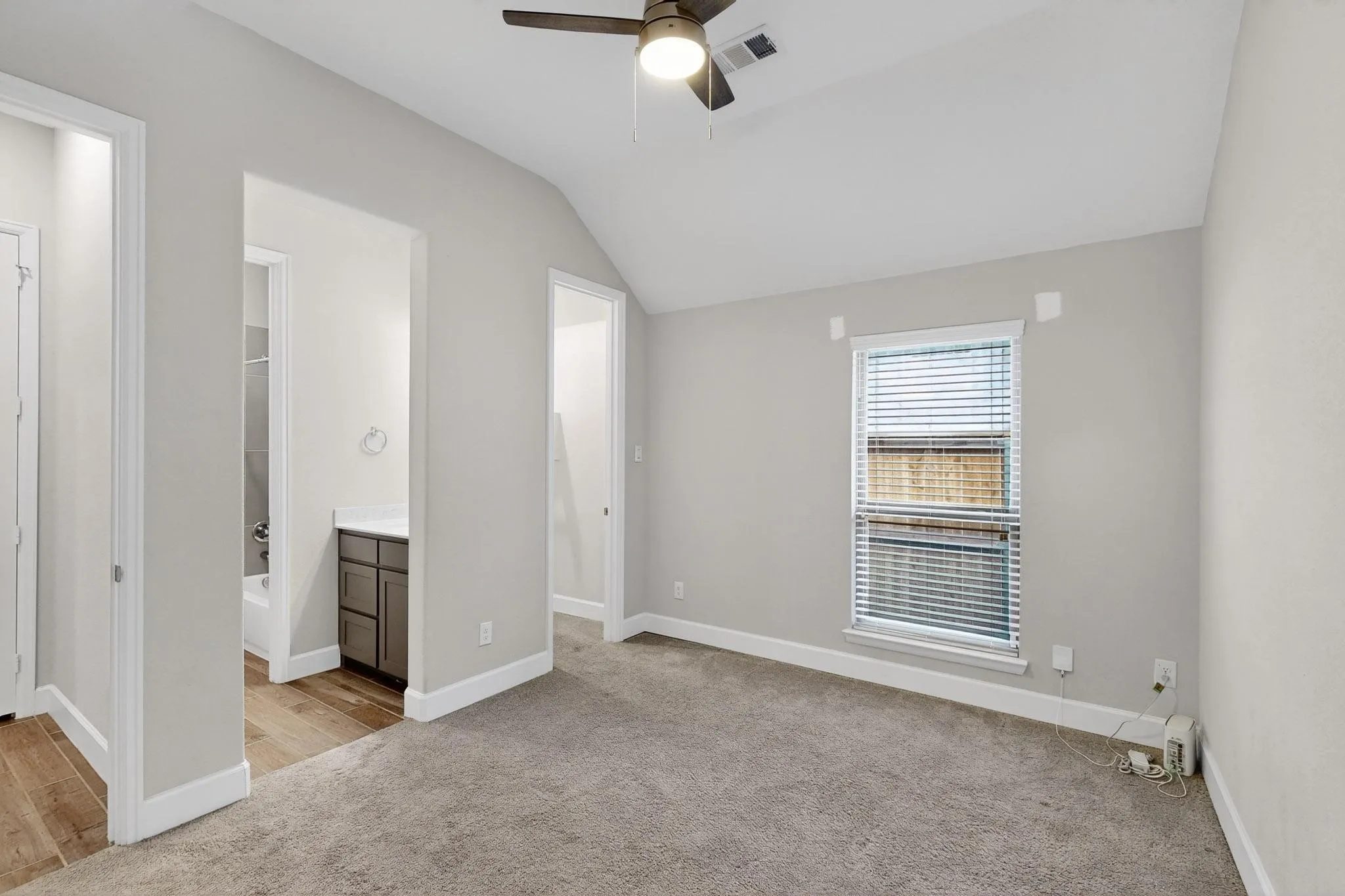 Unfurnished bedroom with lofted ceiling, light colored carpet, ceiling fan, ensuite bathroom, and a walk in closet