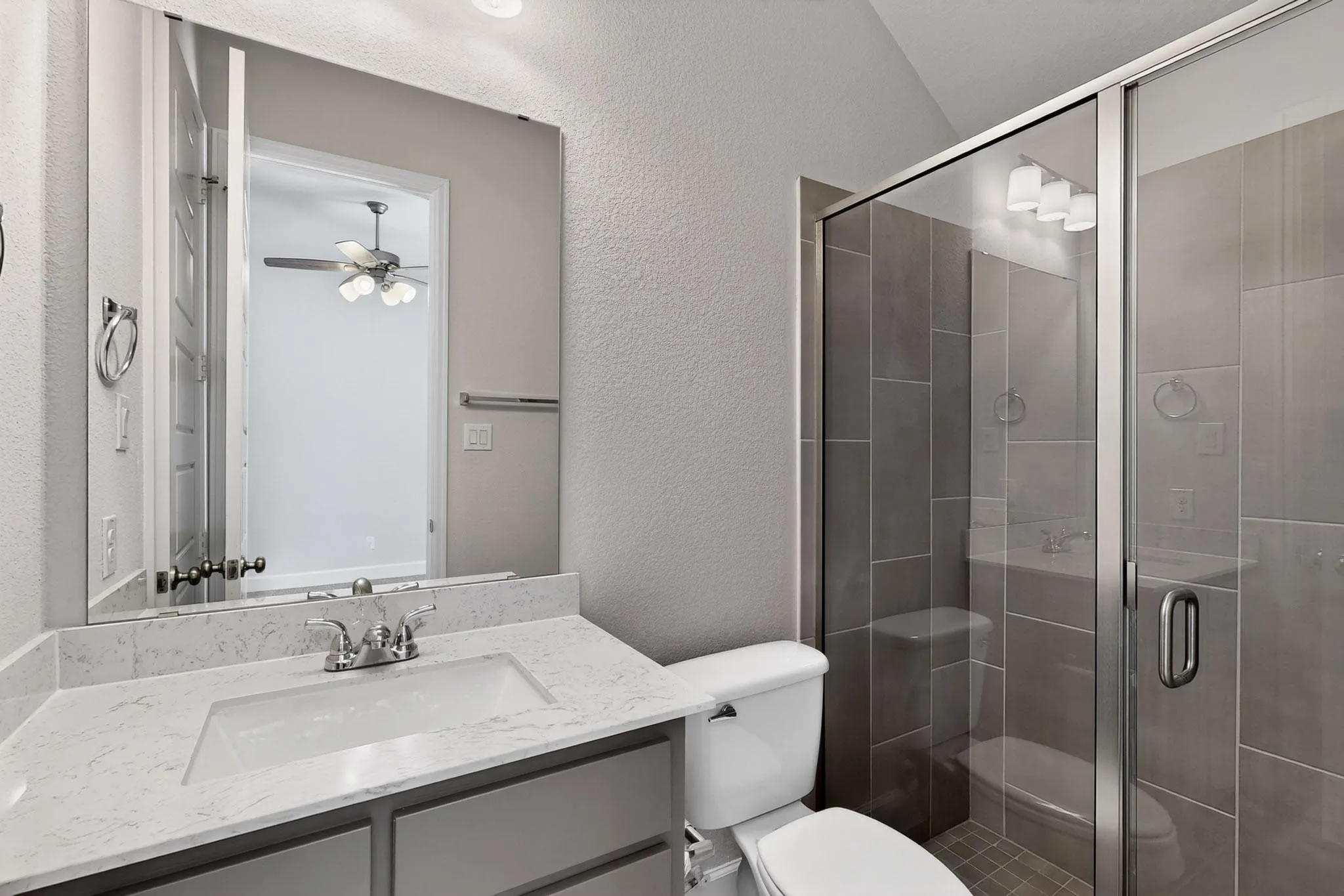 Bathroom with a textured wall, vanity, a shower stall, and ceiling fan