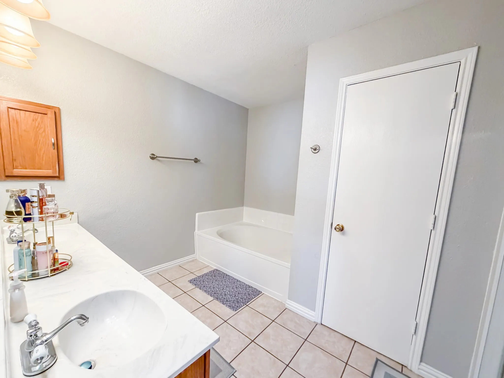 Bathroom featuring a white integrated sink, white countertop, chrome faucet, a built-in bathtub with white surround, and light-toned tile flooring