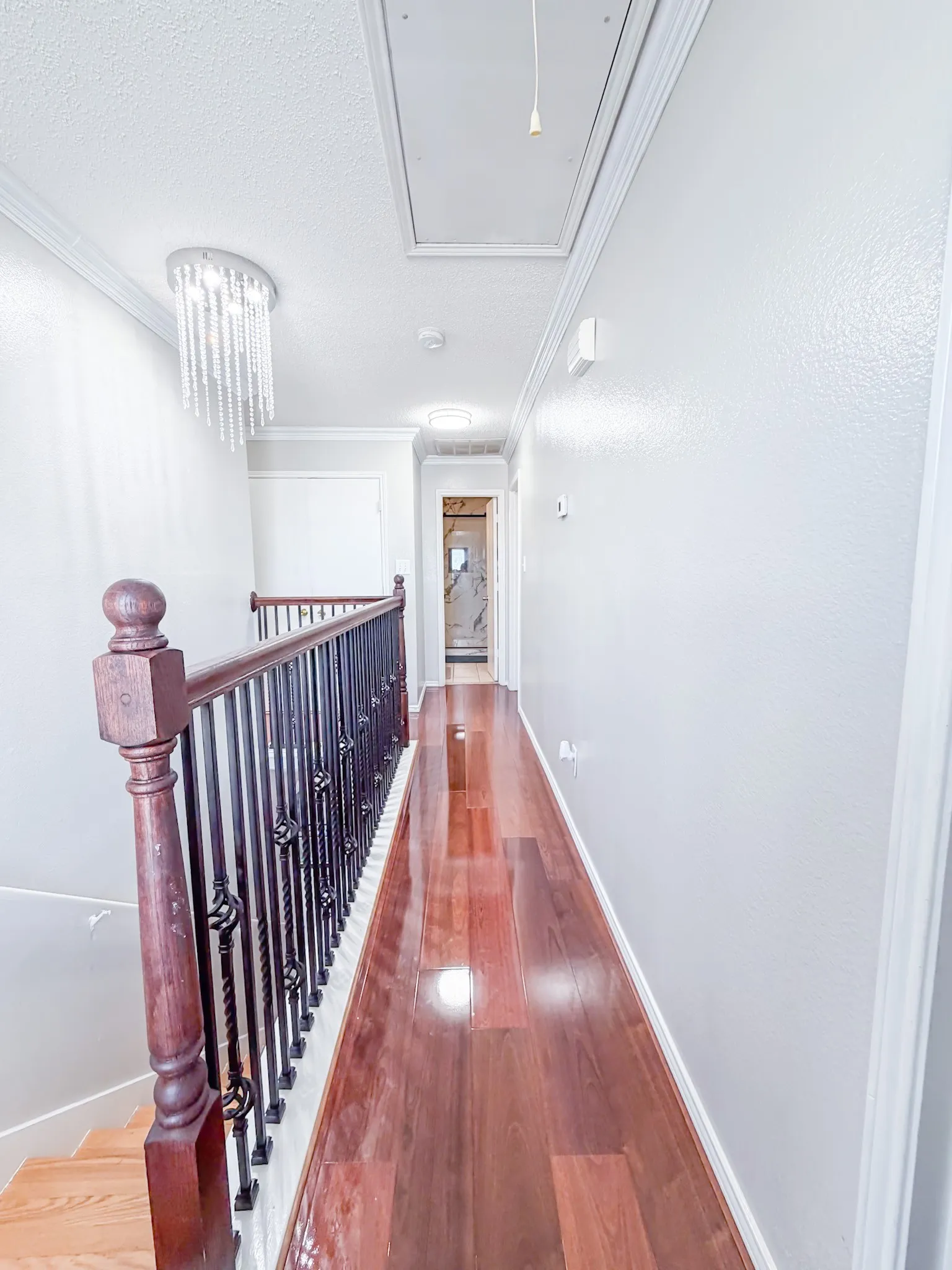 Hallway featuring rich wood-finish flooring, white painted walls, and decorative crown molding