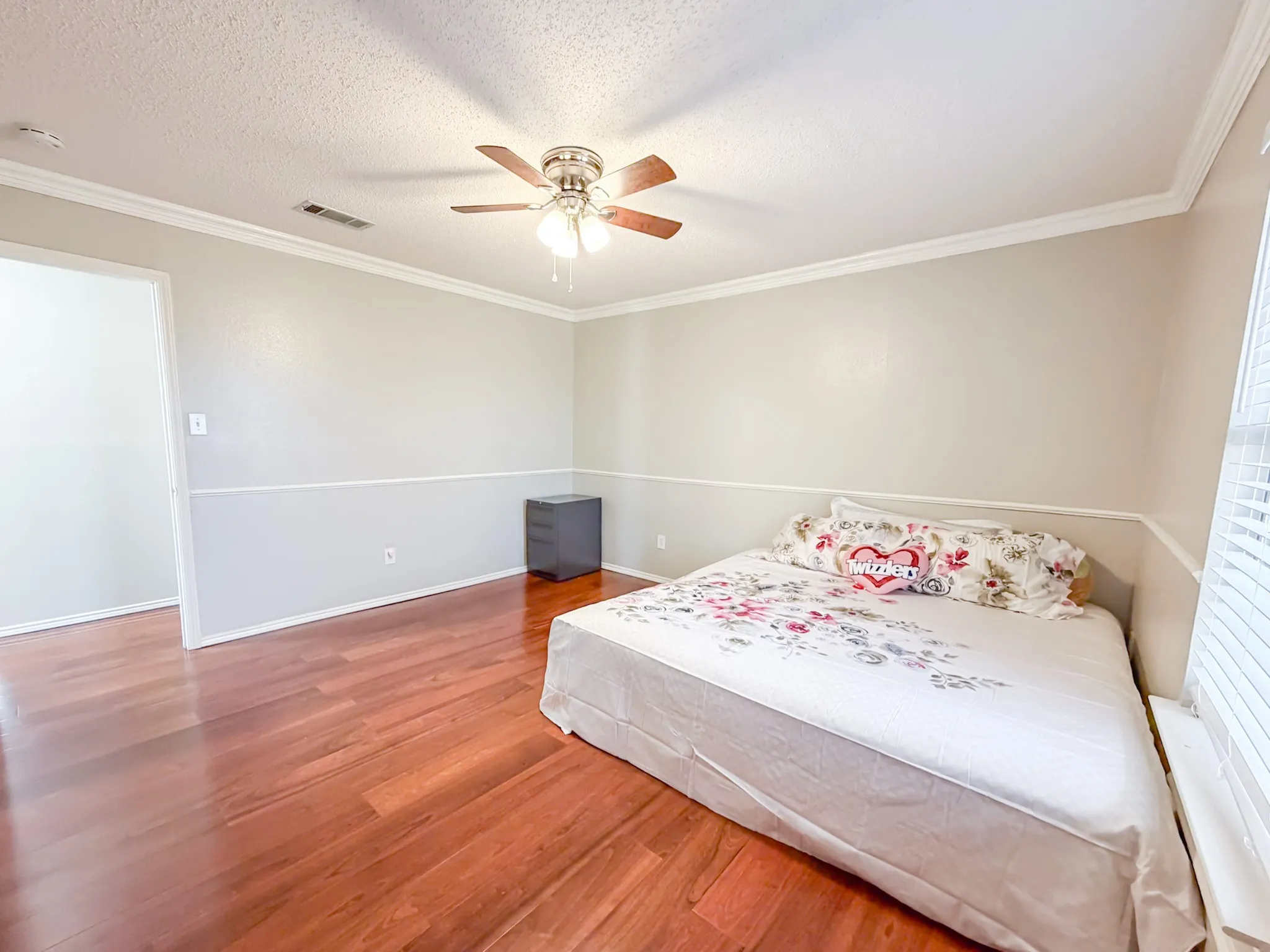Room featuring wood-finish flooring, two-tone wall paint, white crown molding, and a ceiling fan with integrated lighting
