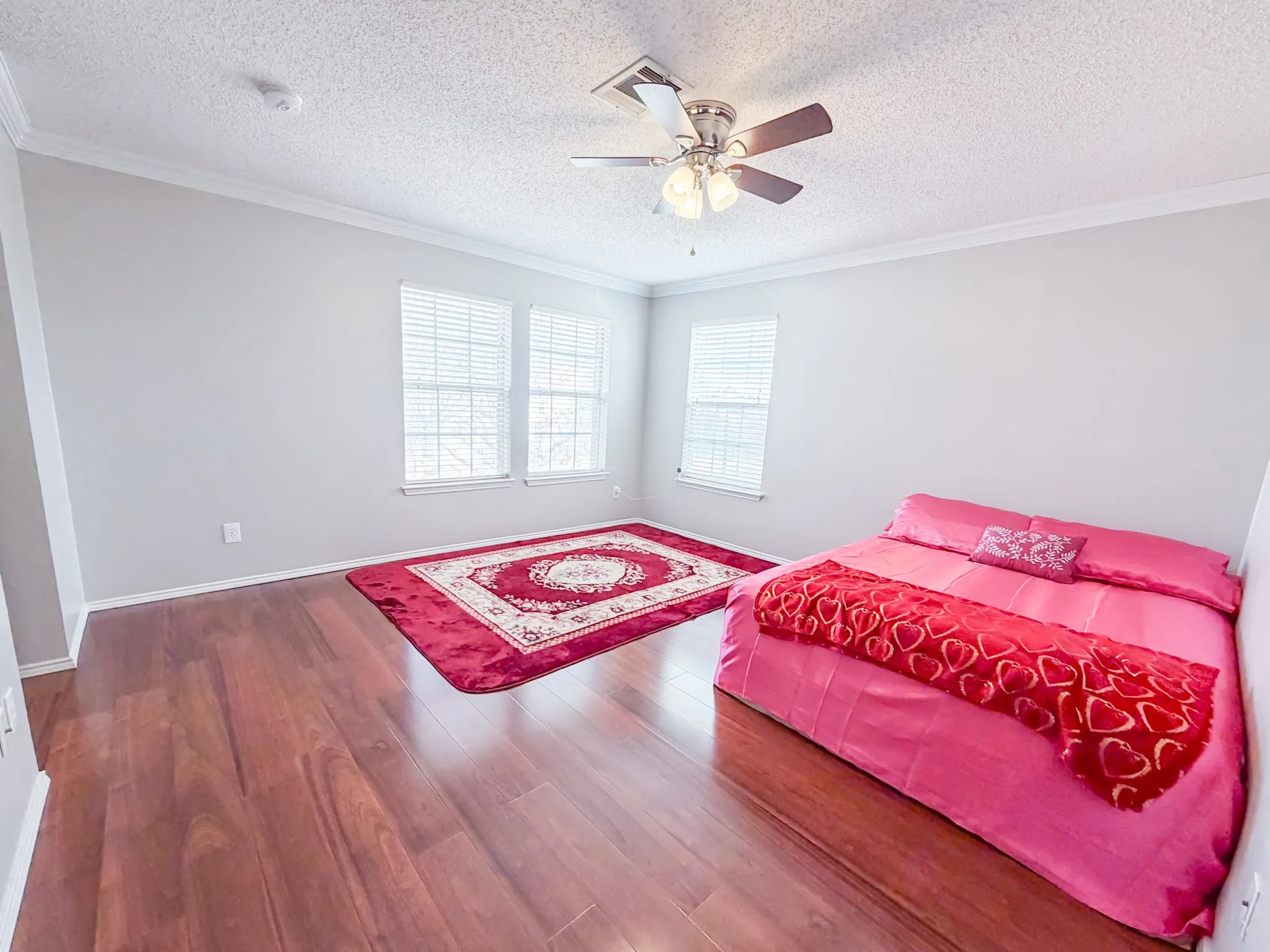 Spacious room featuring wood-finish flooring, two windows with blinds, a ceiling fan with integrated lighting, and crown molding