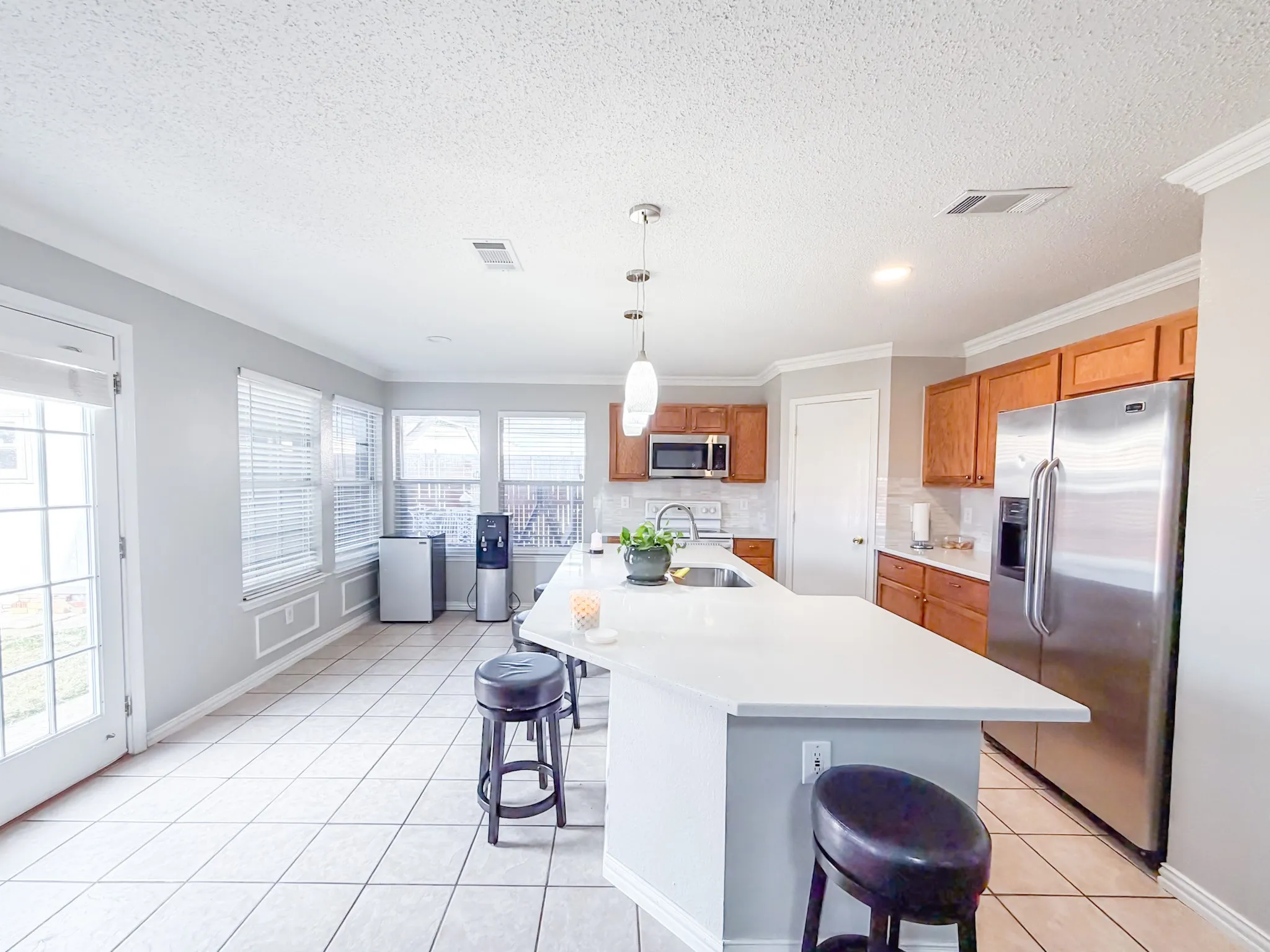 Kitchen featuring a large central island with a white countertop, wood cabinetry, stainless steel appliances, and tile flooring
