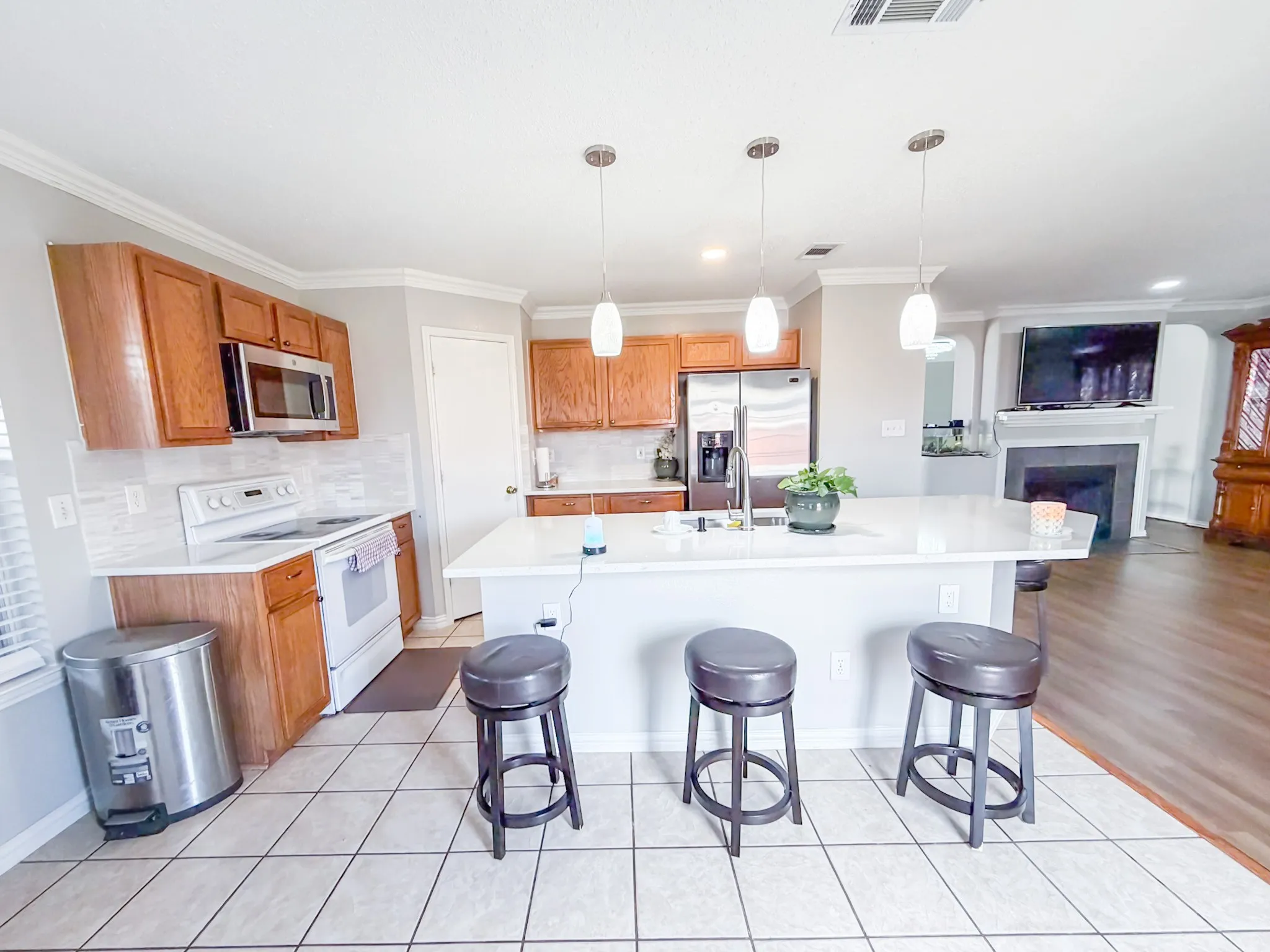 Kitchen featuring a center island with pendant lighting, stainless steel appliances, wood cabinetry, tile backsplash, and tile flooring