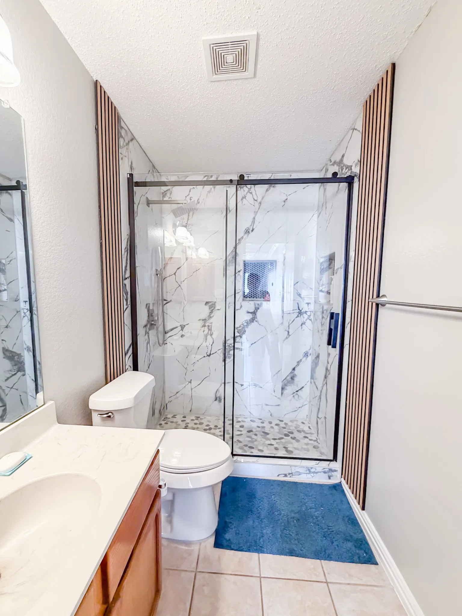Modern bathroom featuring a glass-enclosed shower with marble-look tile, wood-slat accent walls, and a pebble-stone shower floor