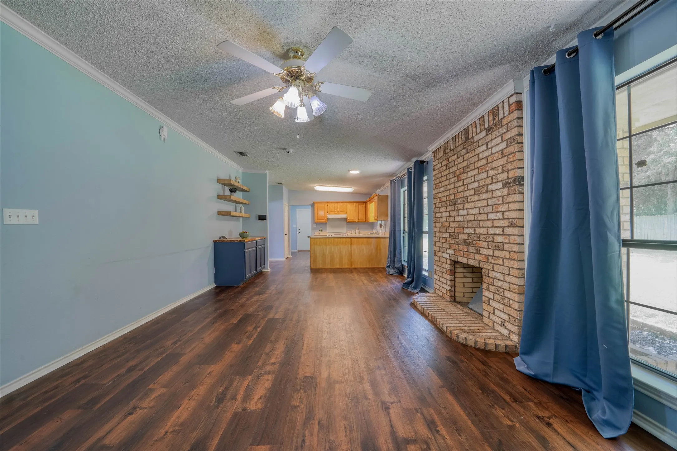 Spacious interior featuring wood-finish flooring, a brick fireplace with hearth, and an open layout towards the kitchen