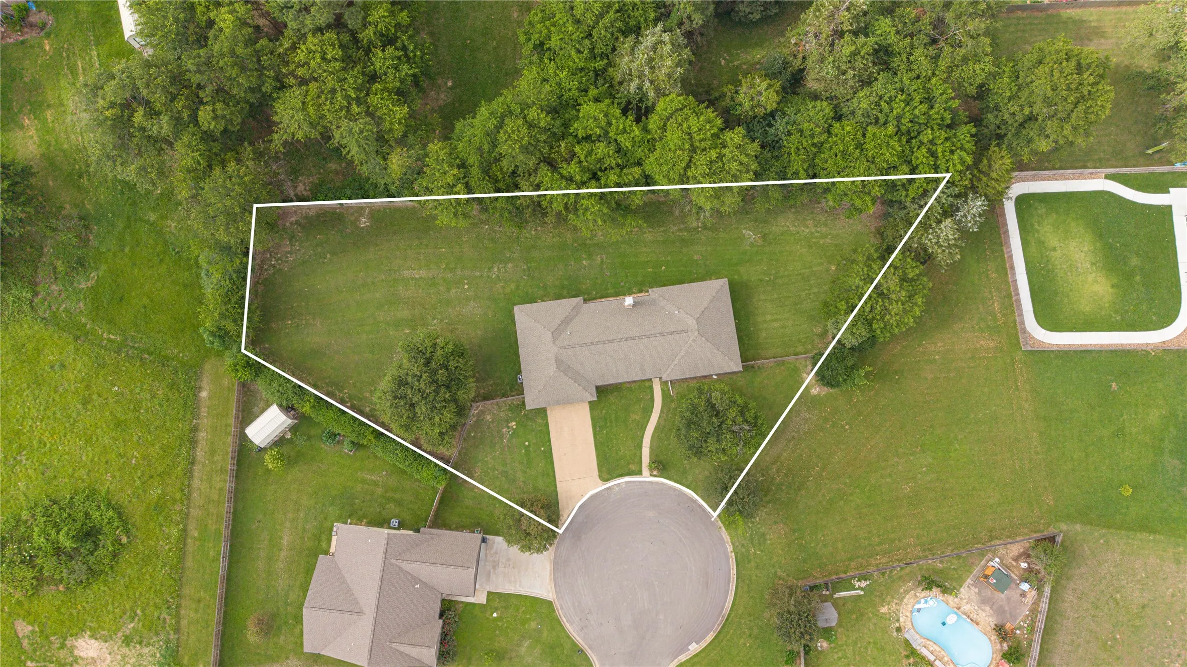 Expansive lot featuring a single-story residence with a pitched roof, mature trees, and a cul-de-sac entrance