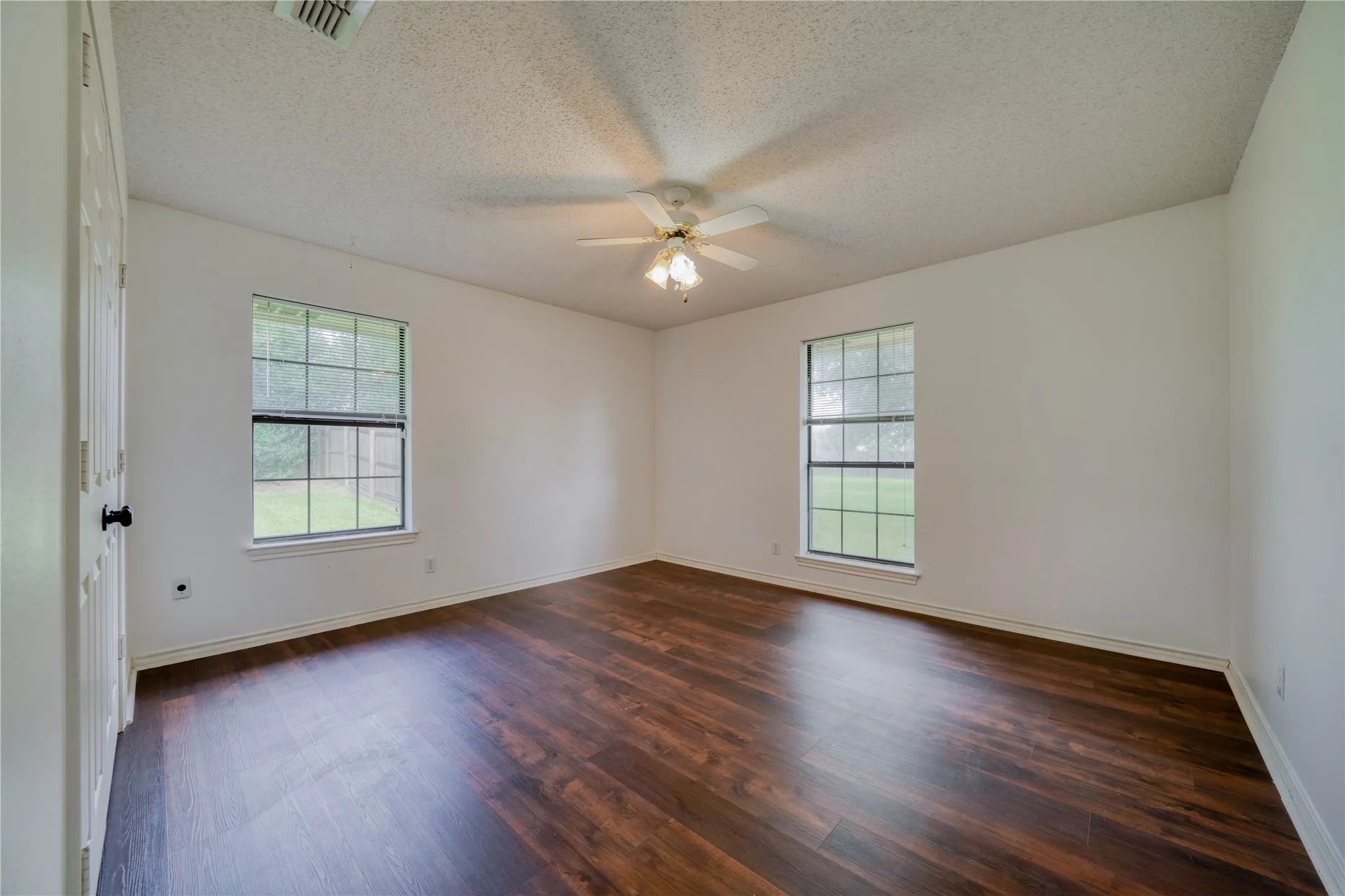 Spacious room featuring wood-finish flooring, white baseboards, and bright white walls