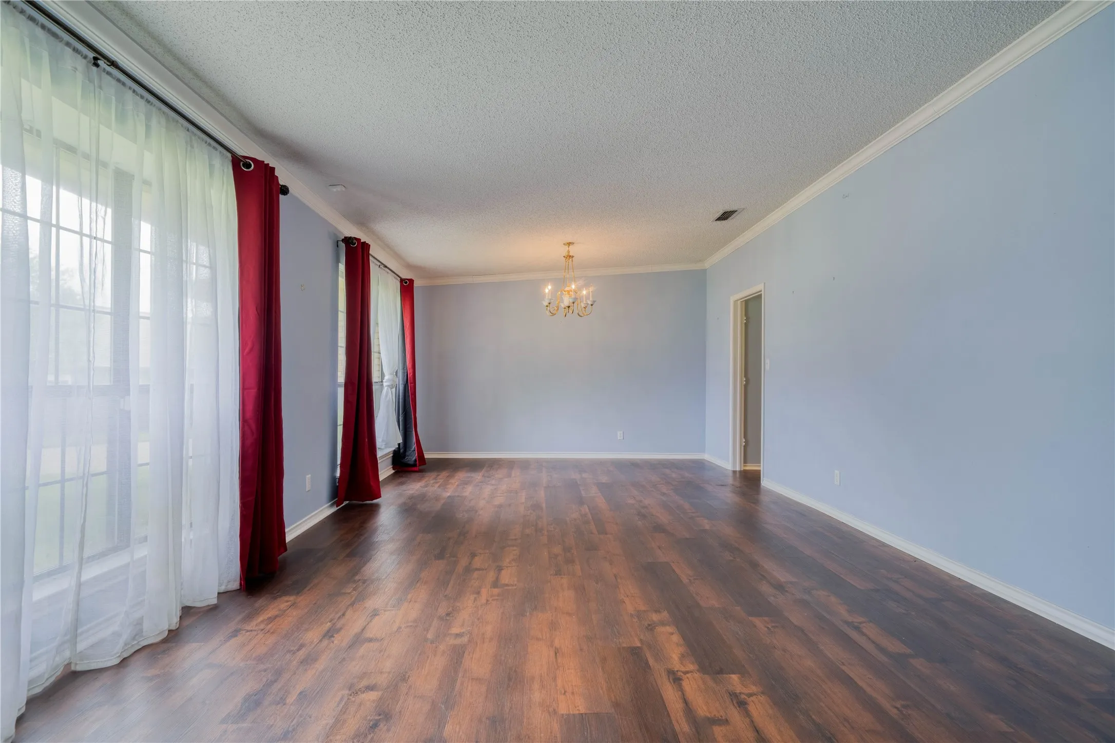 Spacious interior room featuring wood-finish flooring, light blue walls, and white crown molding