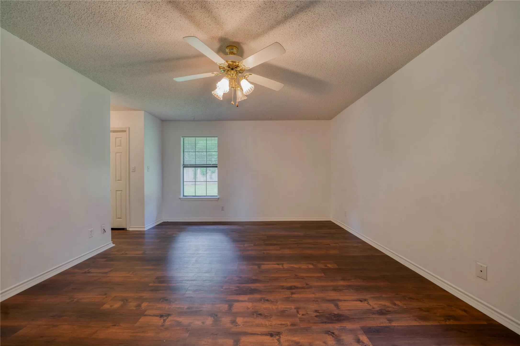 Spacious room featuring wood-finish flooring, white baseboards, and a window with a grid pattern