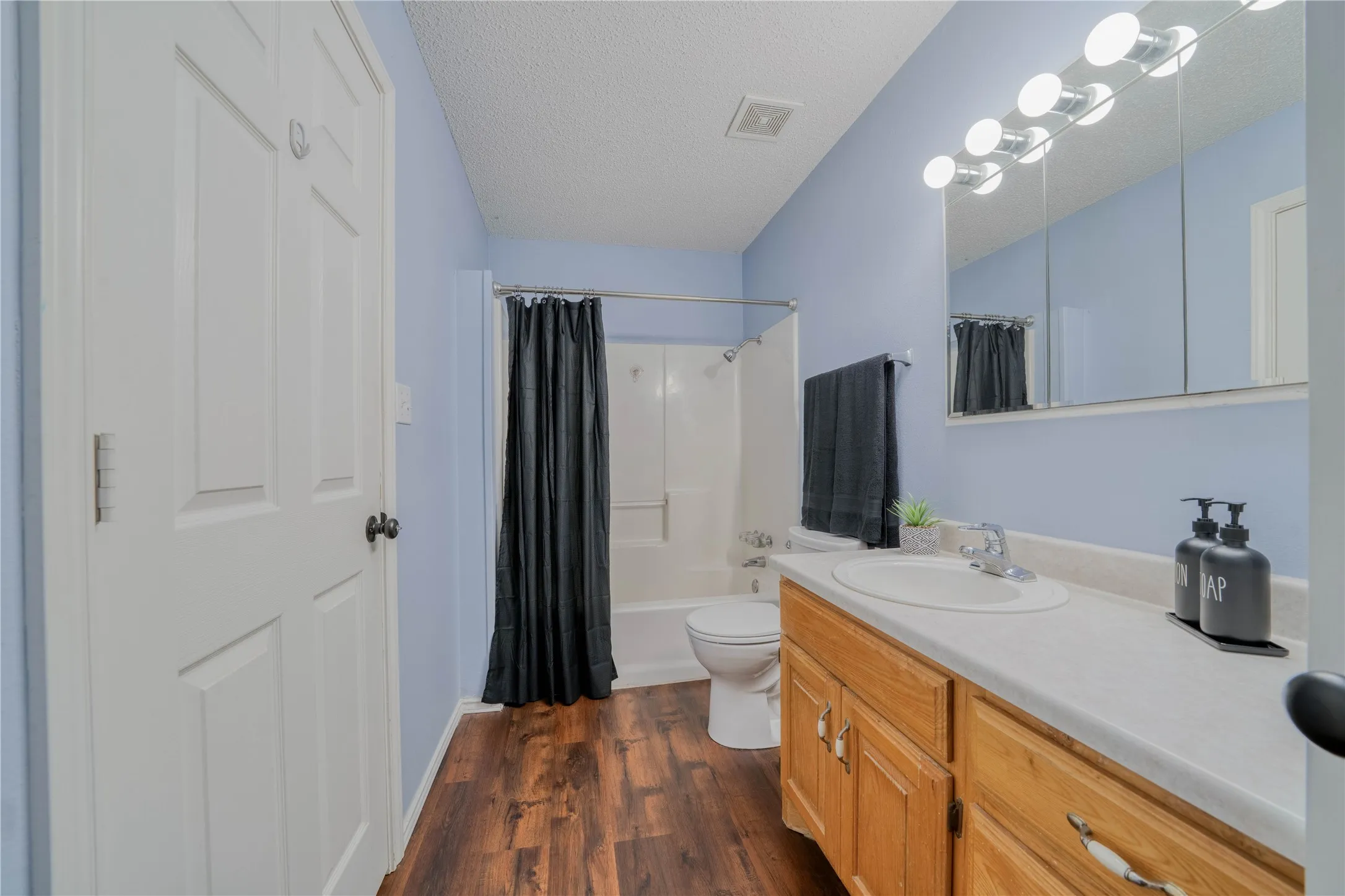 Bathroom featuring wood-finish flooring, light blue walls, and a white vanity with a single sink