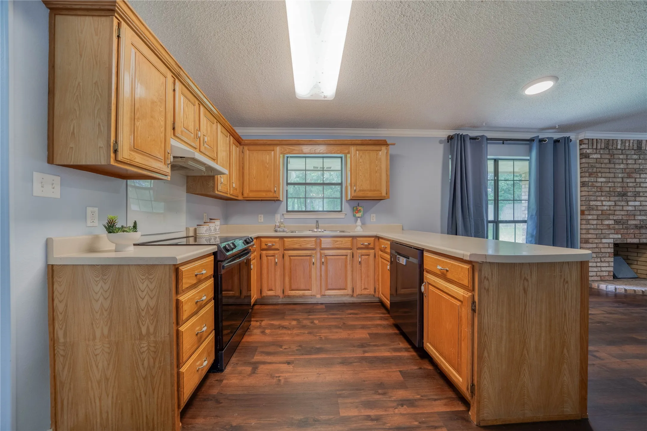U-shaped kitchen featuring wood cabinetry, light-toned countertops, and wood-finish flooring