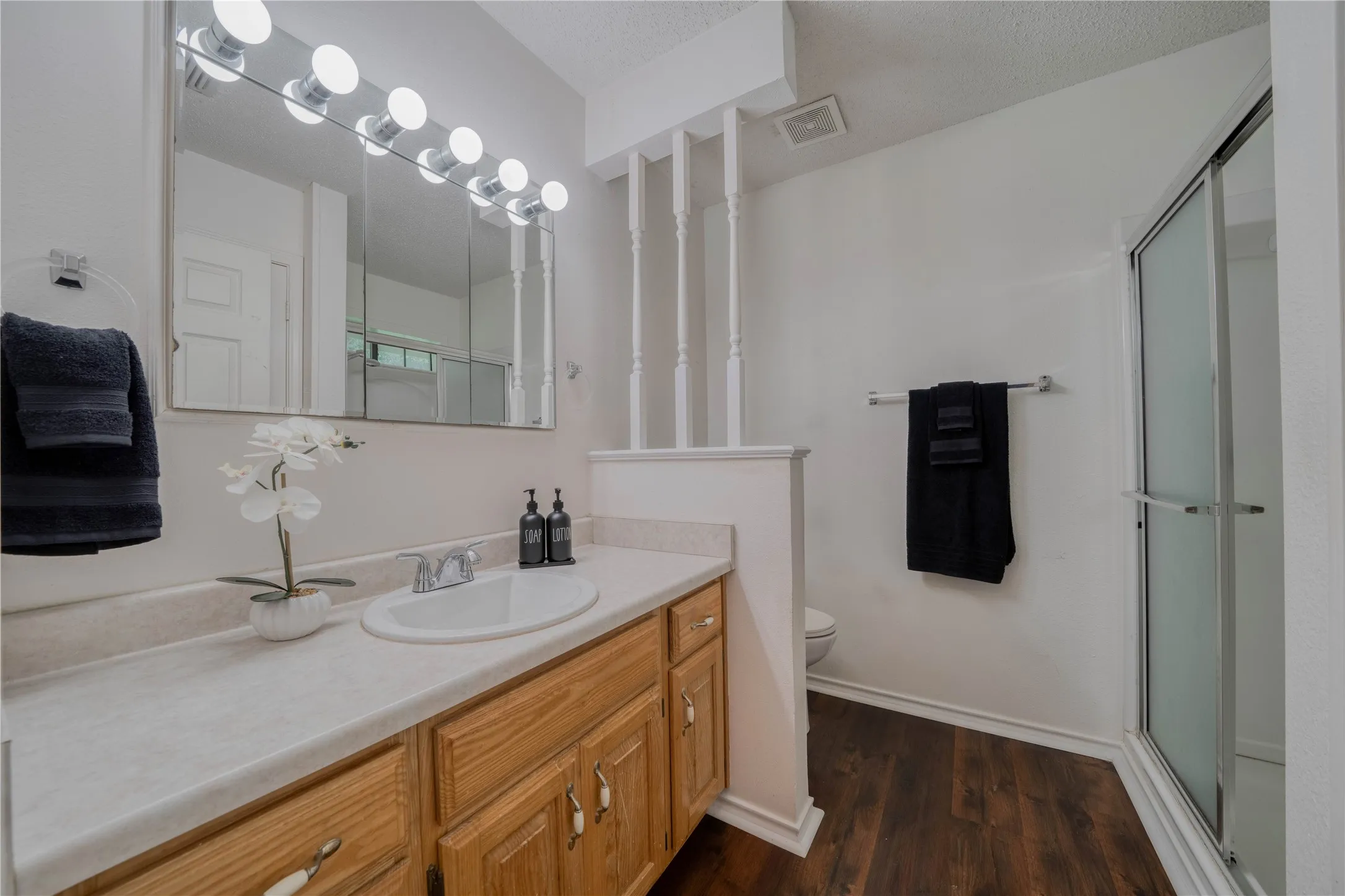 Bathroom featuring a single vanity with wood-finish cabinetry and an integrated sink, a mirrored medicine cabinet with strip lighting, a walk-in shower with a frosted glass enclosure, and wood-finish flooring