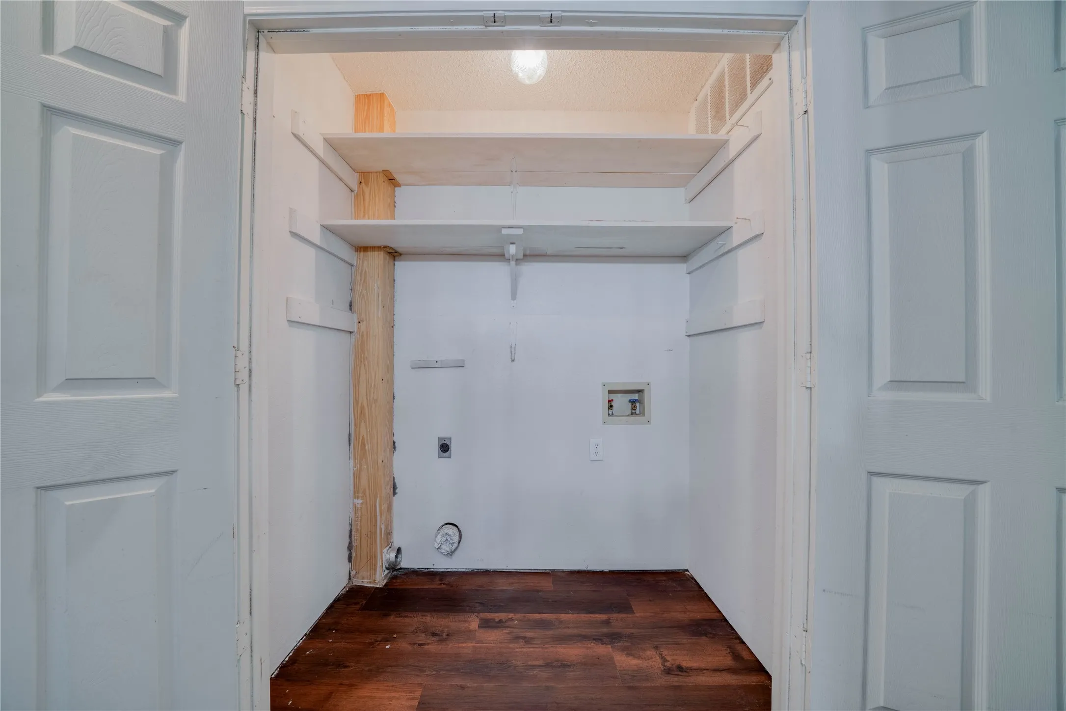 Laundry closet featuring wood-finish flooring, two white panel doors, and built-in shelving