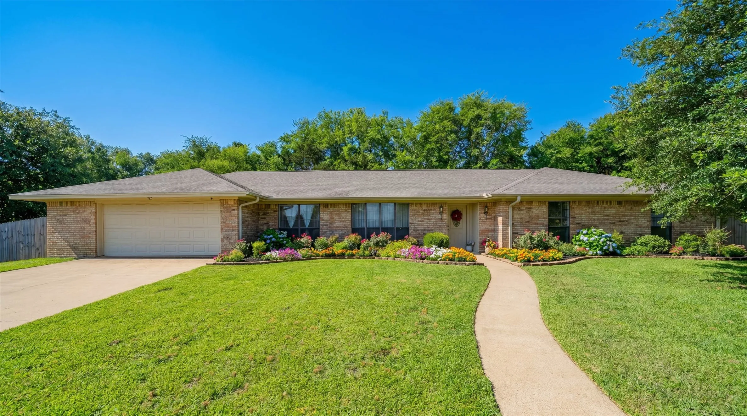 Traditional brick facade featuring a two-car garage, concrete driveway, and a curved sidewalk