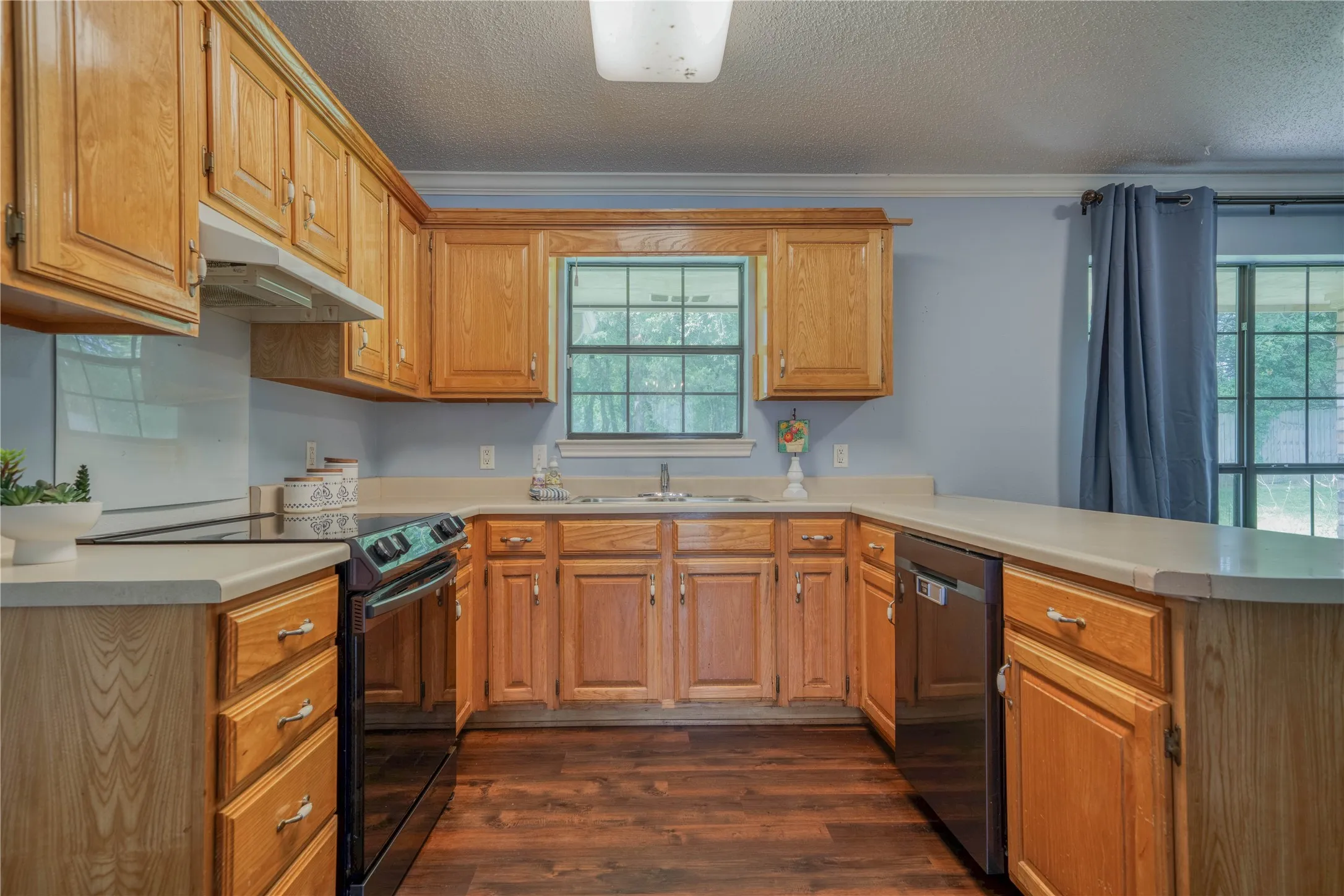 Kitchen featuring wood cabinetry, light countertops, dark wood-finish flooring, a black electric range, and a black dishwasher