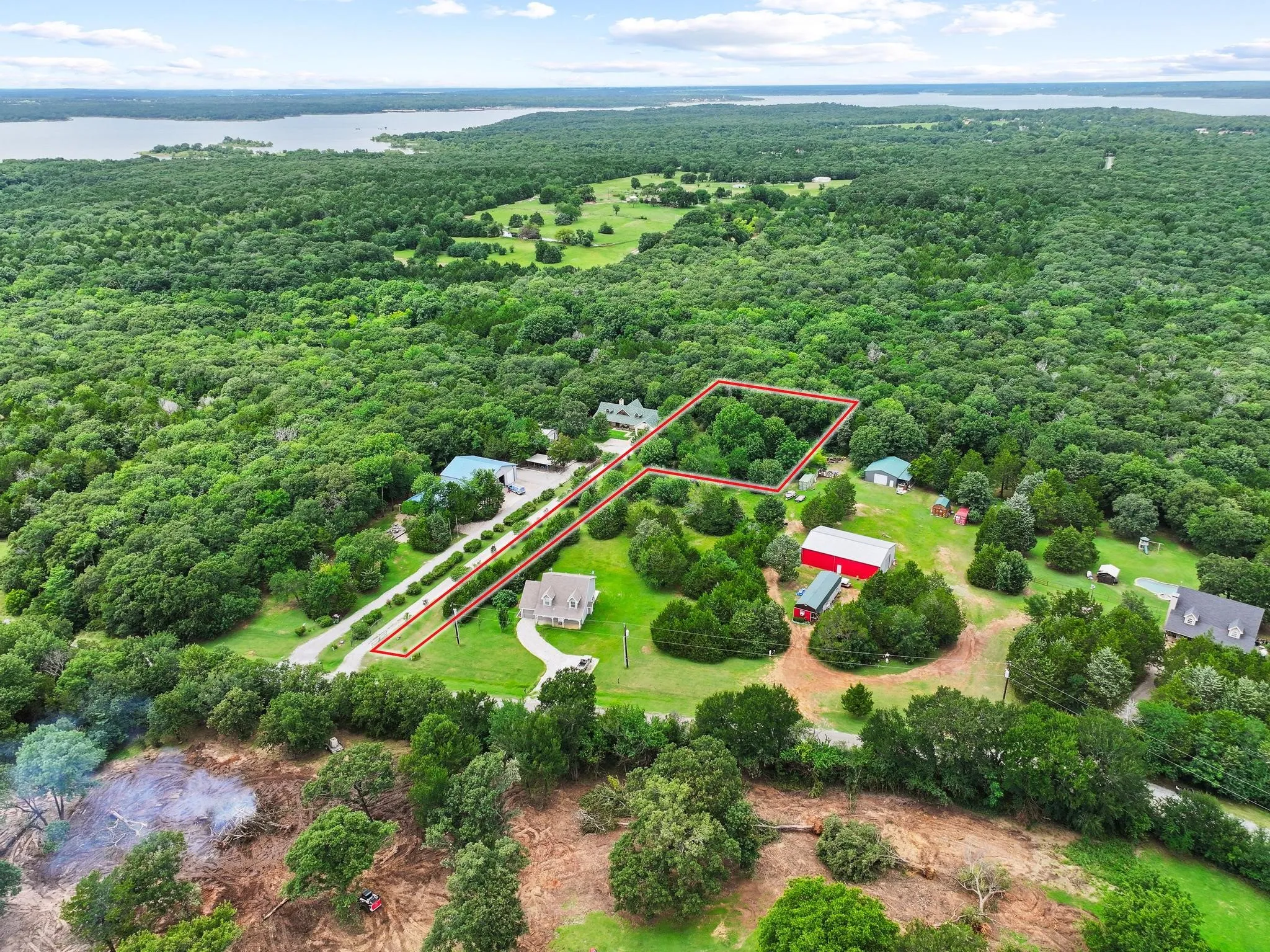 Aerial perspective showcasing a property outlined in red, featuring a drive, mature trees, and proximity to a large body of water
