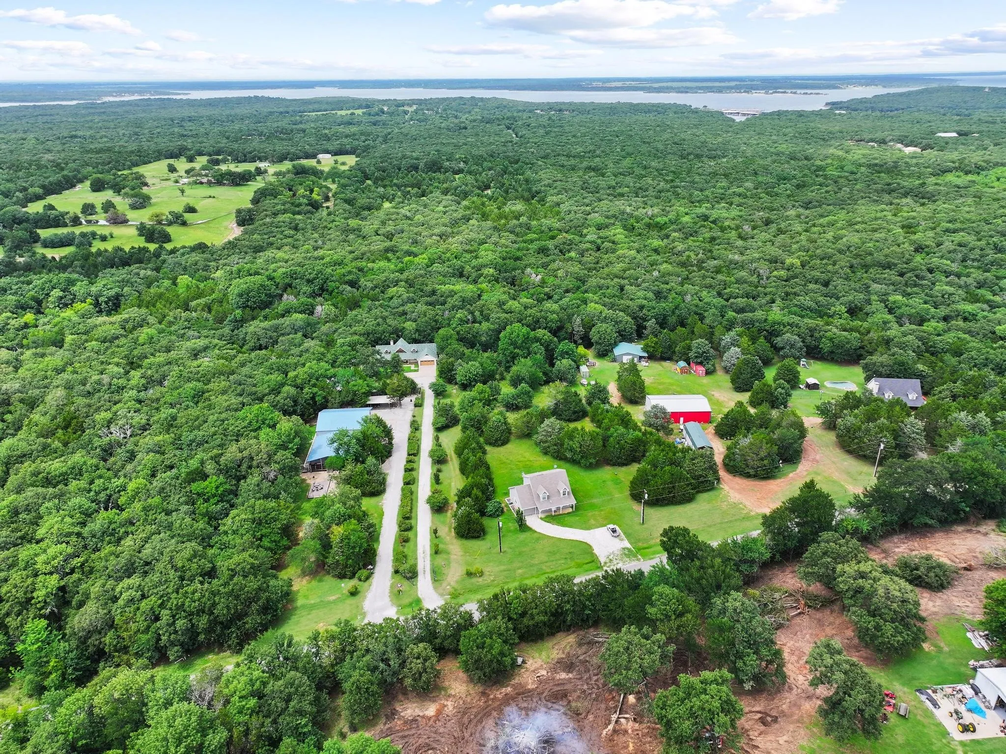 Expansive property featuring dense tree coverage, multiple structures, a prominent main residence with a circular drive, and an extended private driveway