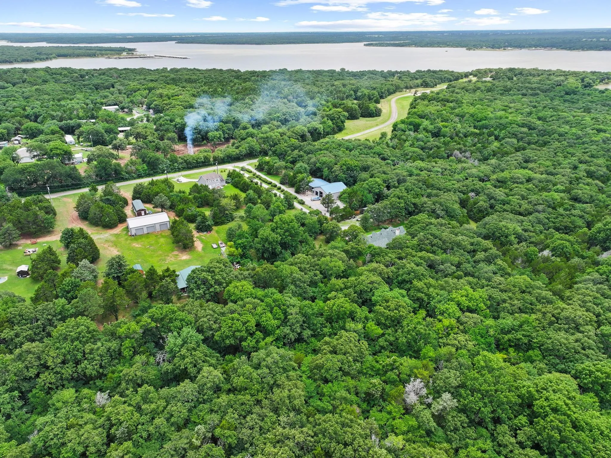 Expansive aerial view showcasing a large body of water, extensive wooded acreage, and multiple buildings