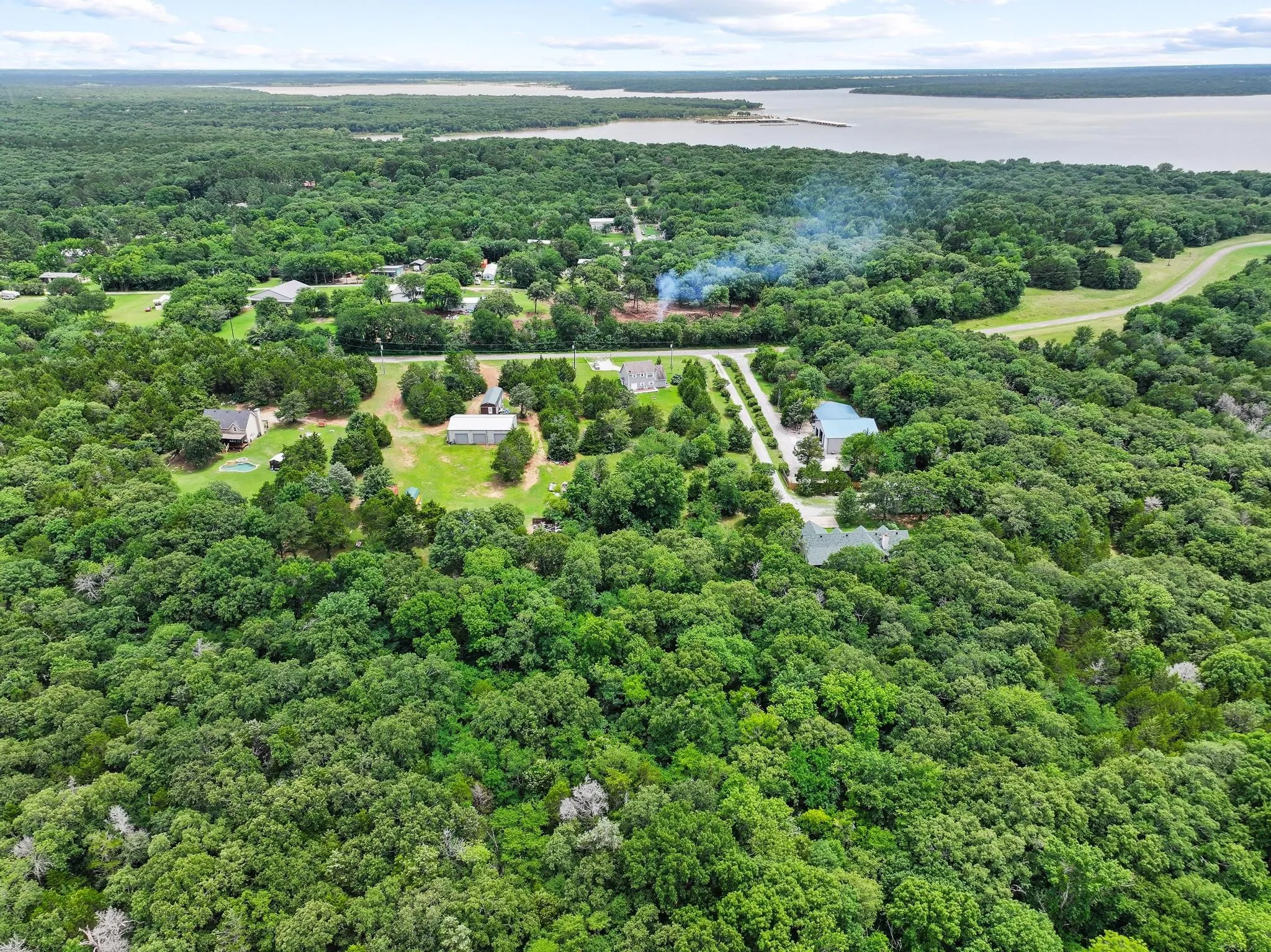 Expansive wooded property featuring a lake in the background, multiple residential structures, and established roadways