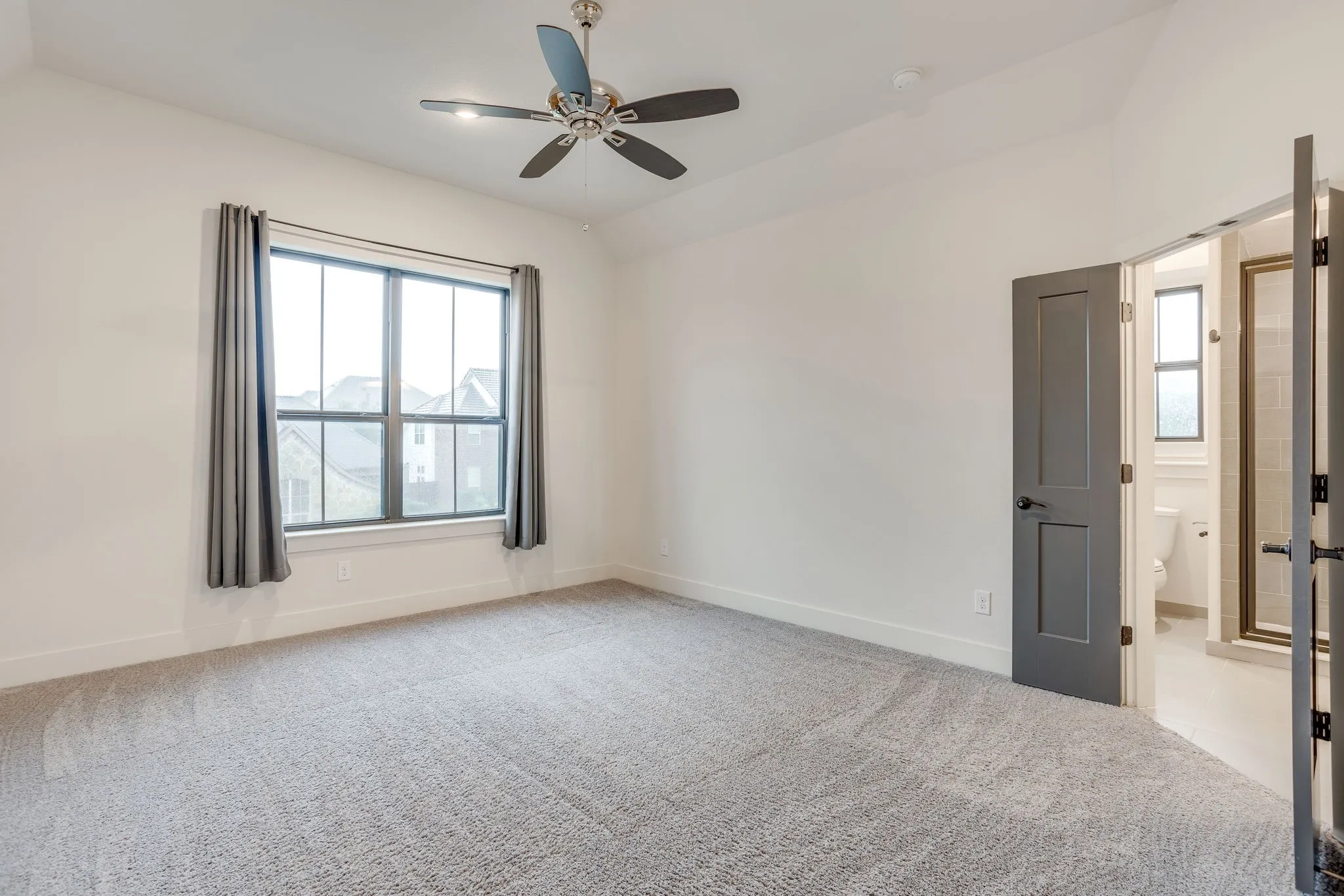 Bedroom 4 Spacious room featuring vaulted ceilings, a large multi-pane window with dark trim, gray carpeting, and a ceiling fan