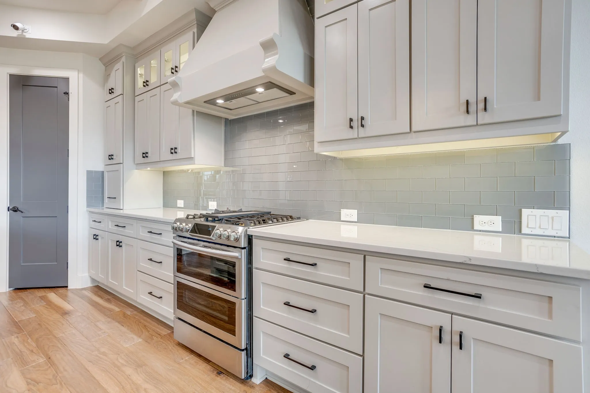 Kitchen featuring shaker-style cabinetry, quartz countertops, a subway tile backsplash, stainless steel range with double ovens, and wood-finish flooring