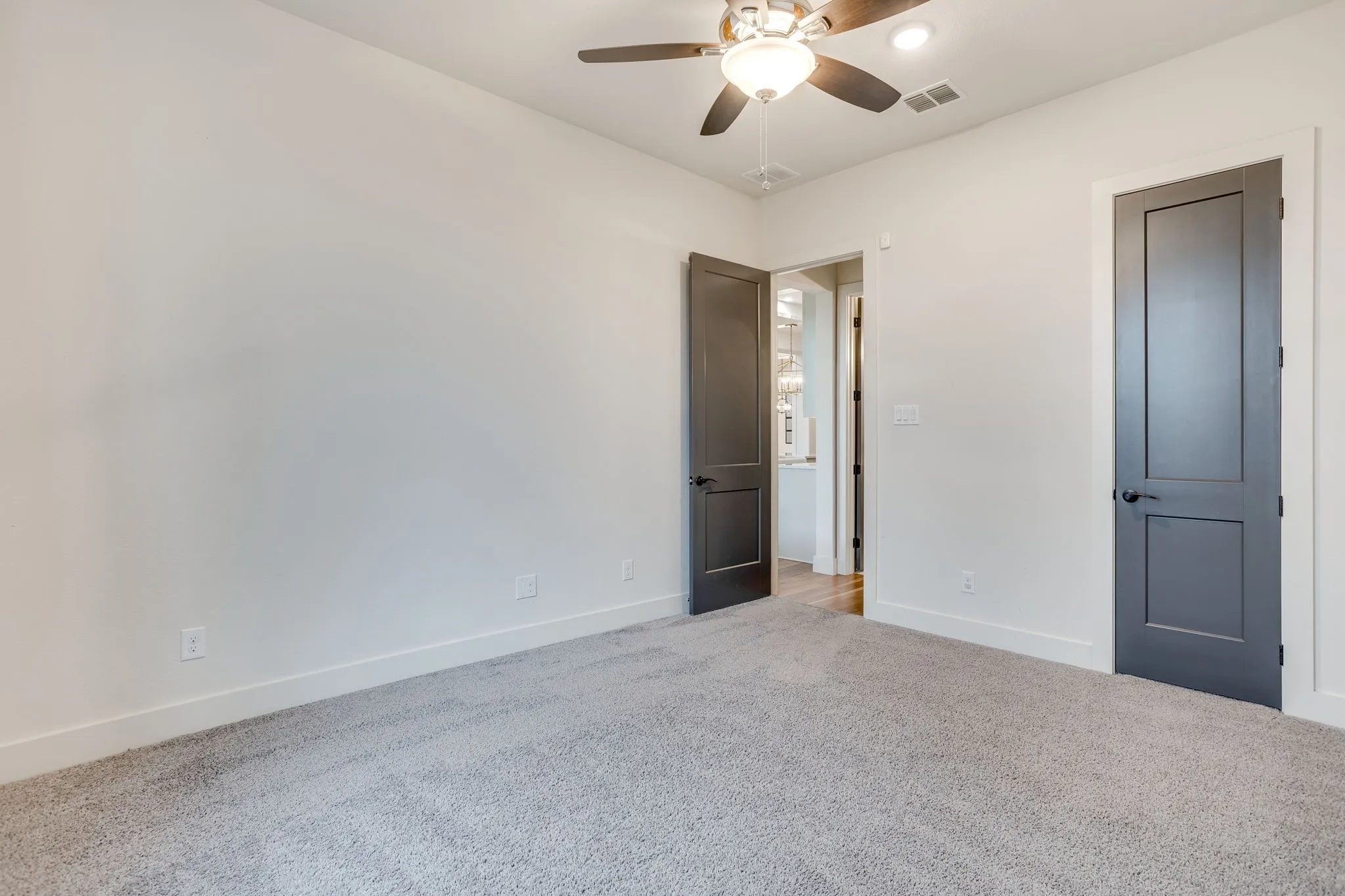 Bedroom #2 Carpeted interior room featuring light-colored walls, white baseboards, and dark-paneled doors with black hardware