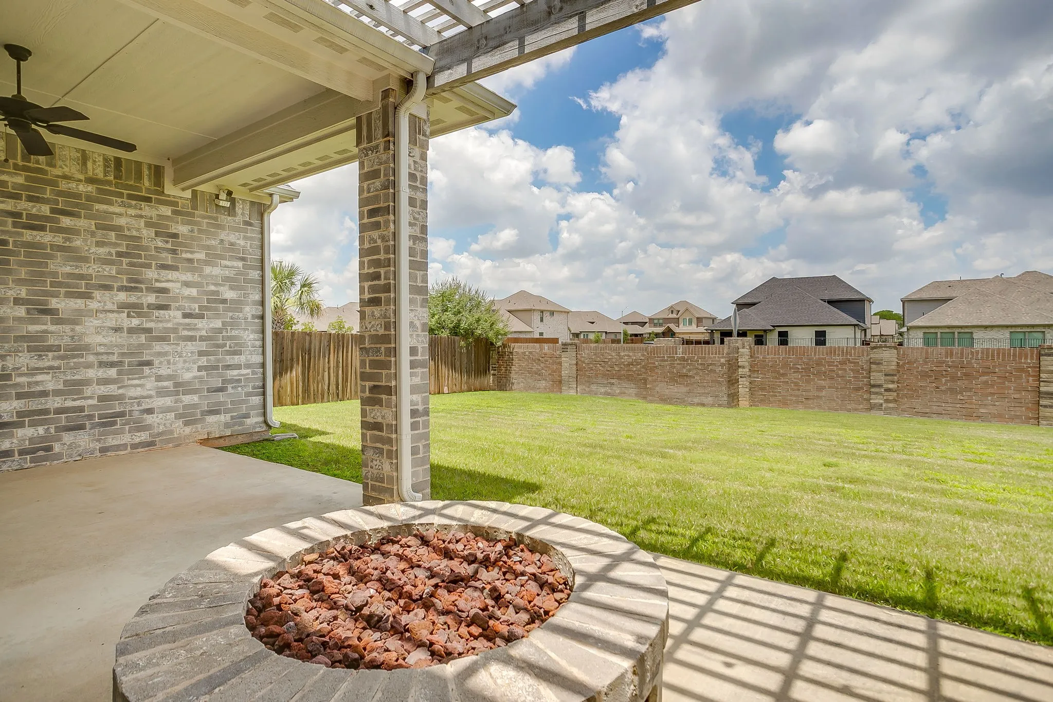 Back Patio featuring primary accent walls and support columns wrapped in multi-colored brick, circular fire pit, enclosed property line with brick privacy wall.