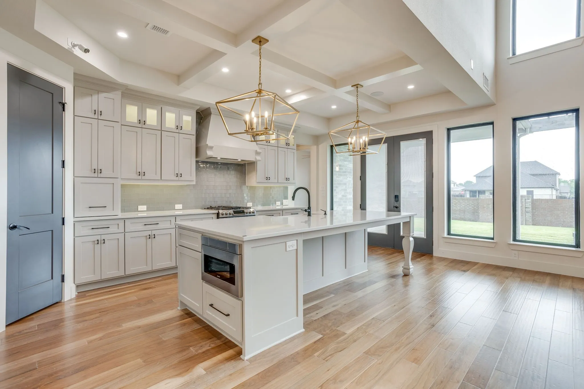 Gourmet kitchen featuring a large central island with integrated microwave, extensive light-toned cabinetry, quartz countertops, and decorative pendant lighting fixtures