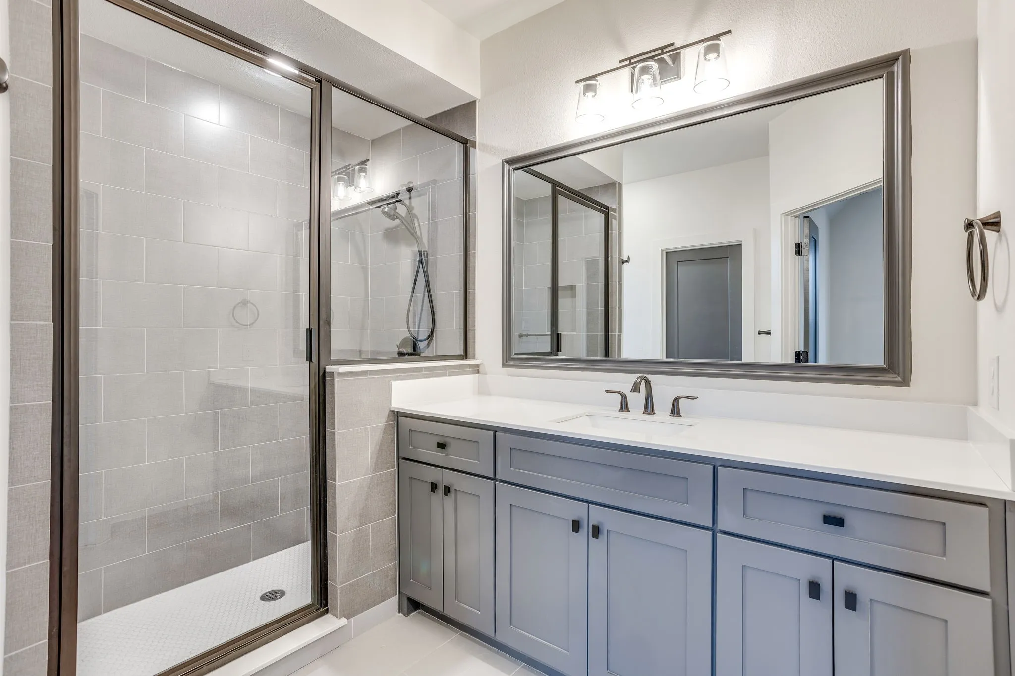 Gray shaker cabinetry with black hardware, white countertop, rectangular undermount sink, and dark-framed mirror