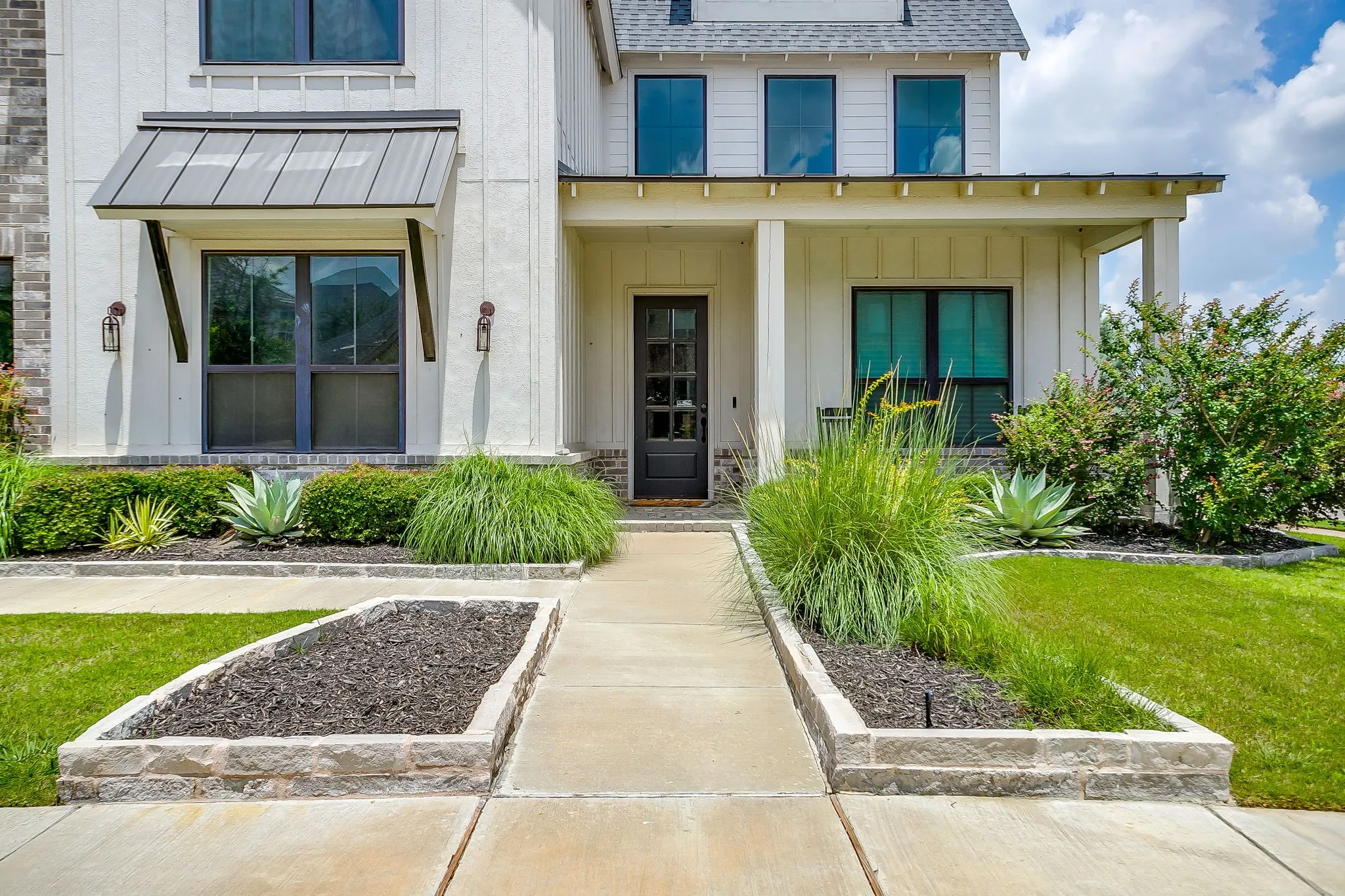 Front entry of house featuring modern farmhouse architectural style with board-and-batten siding and low level brick and open soffit design over the front porch.