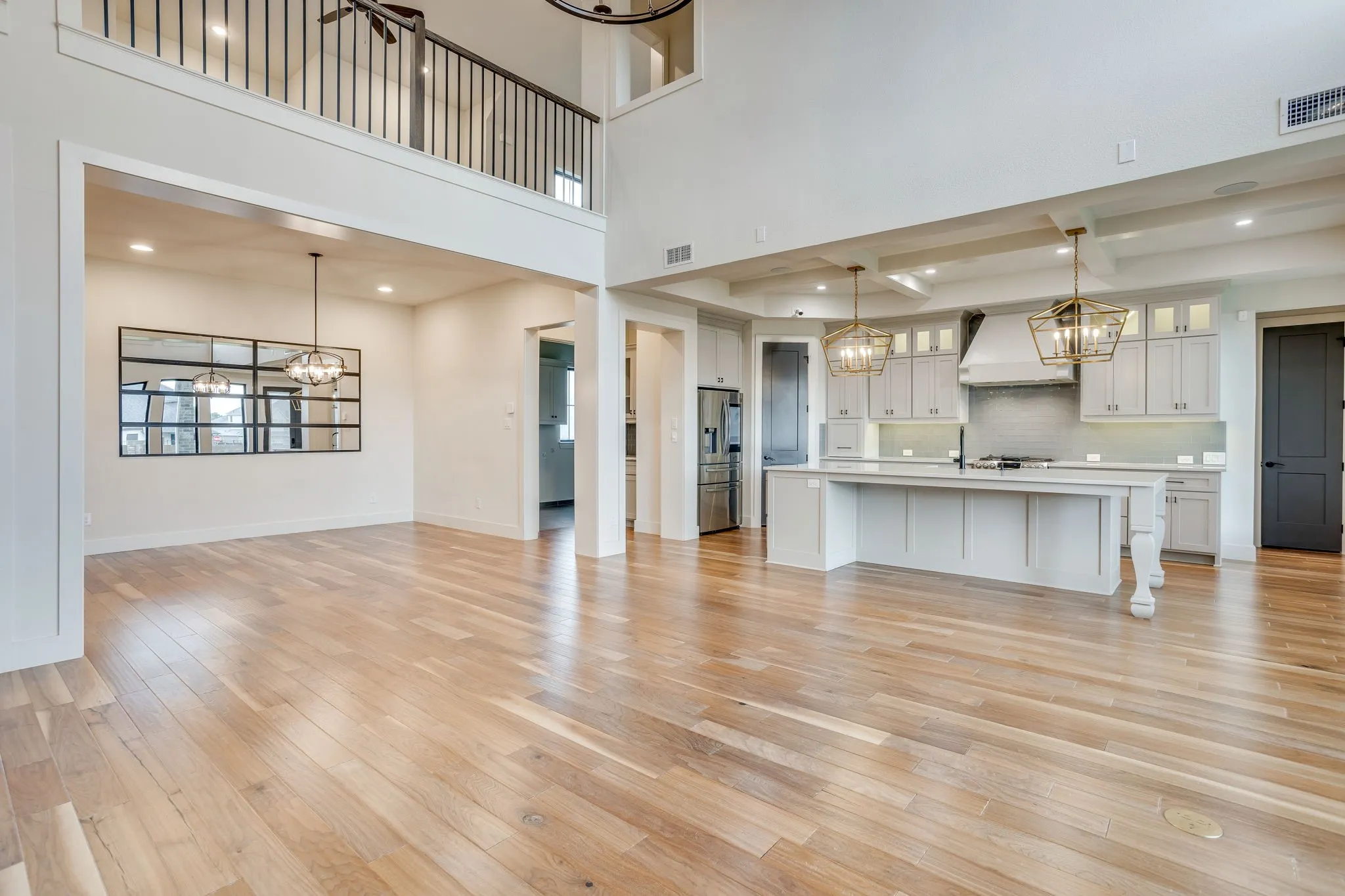 Spacious interior featuring wood-finish flooring, a two-story ceiling, and a kitchen with an oversized island and pendant lighting