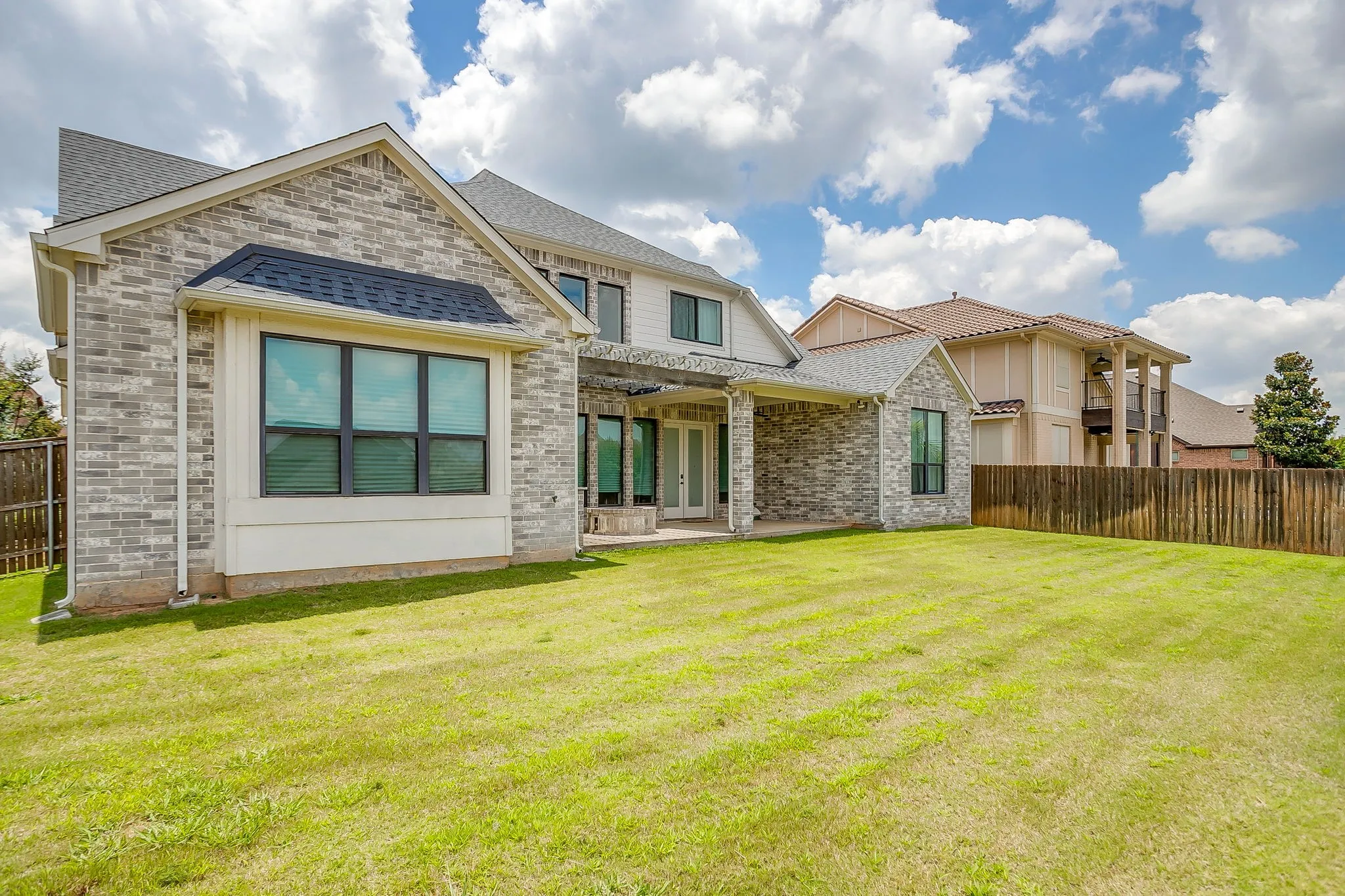 Back of structure featuring multi-toned brick, modern windows with dark charcoal frames and covered back patio.