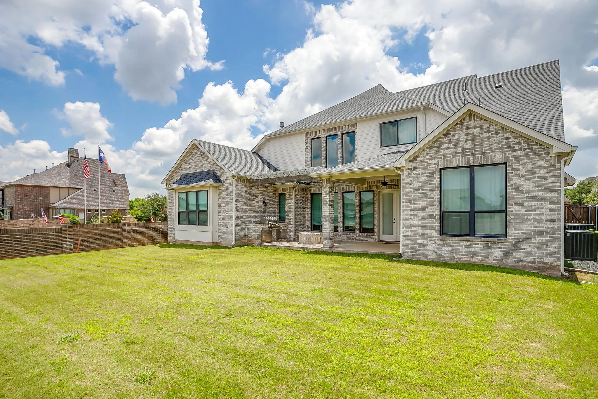 Back of house featuring board-and-batten siding on the second level and multi-colored neutral toned brick on the first level with windows finished in a dark contrasting trim color.