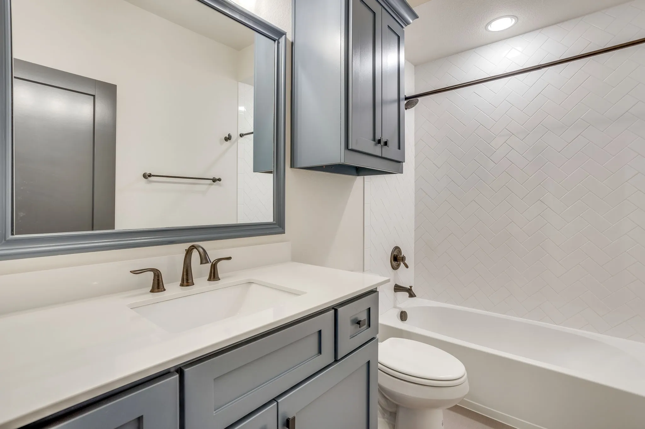 Bathroom featuring a tub/shower combination with white herringbone tile surround, a built-in vanity with gray cabinetry, white countertop, and an integrated sink with a bronze-finish faucet