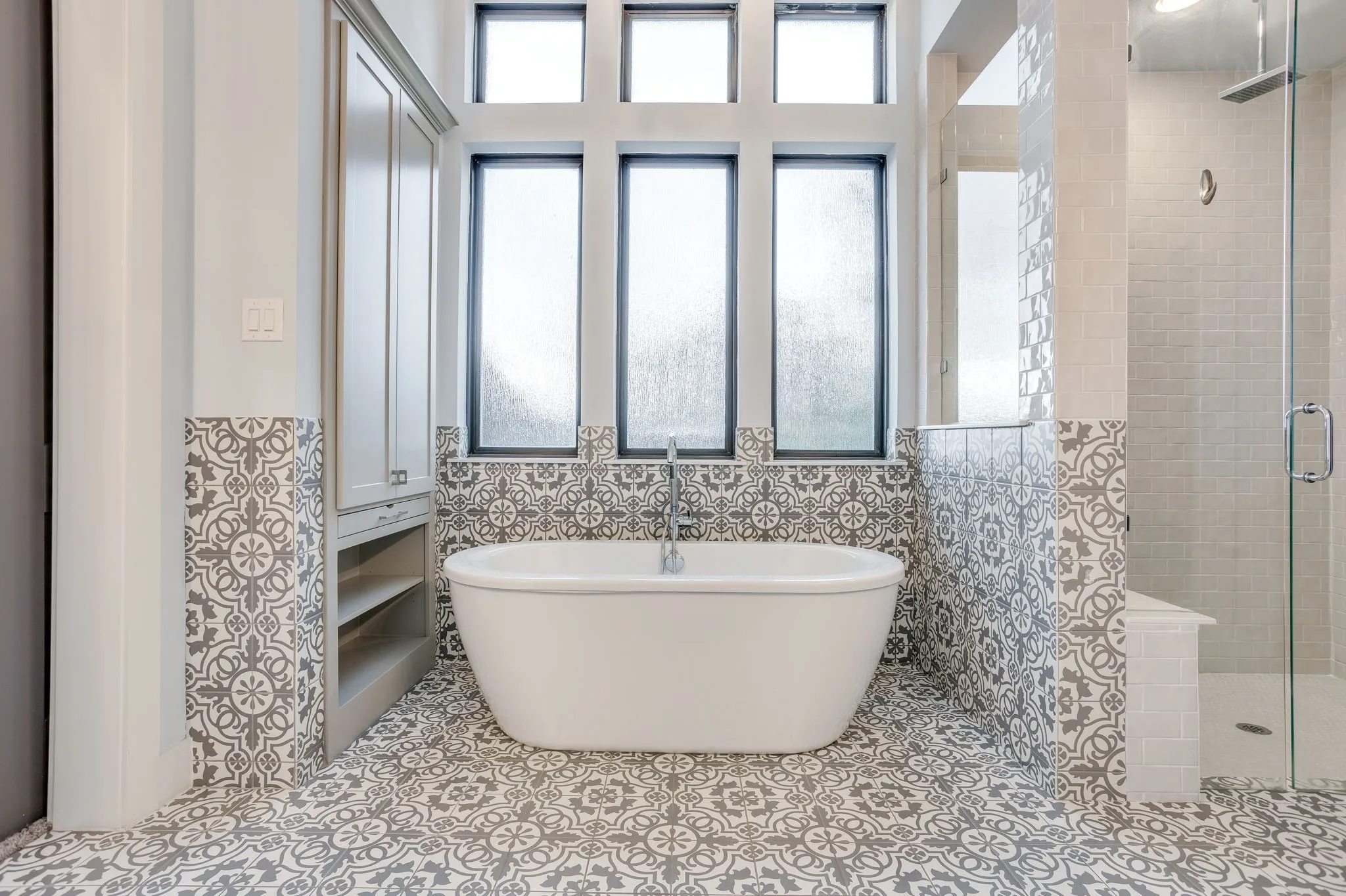 Freestanding soaking tub with a floor-mounted faucet, complemented by patterned floor and accent wall tile