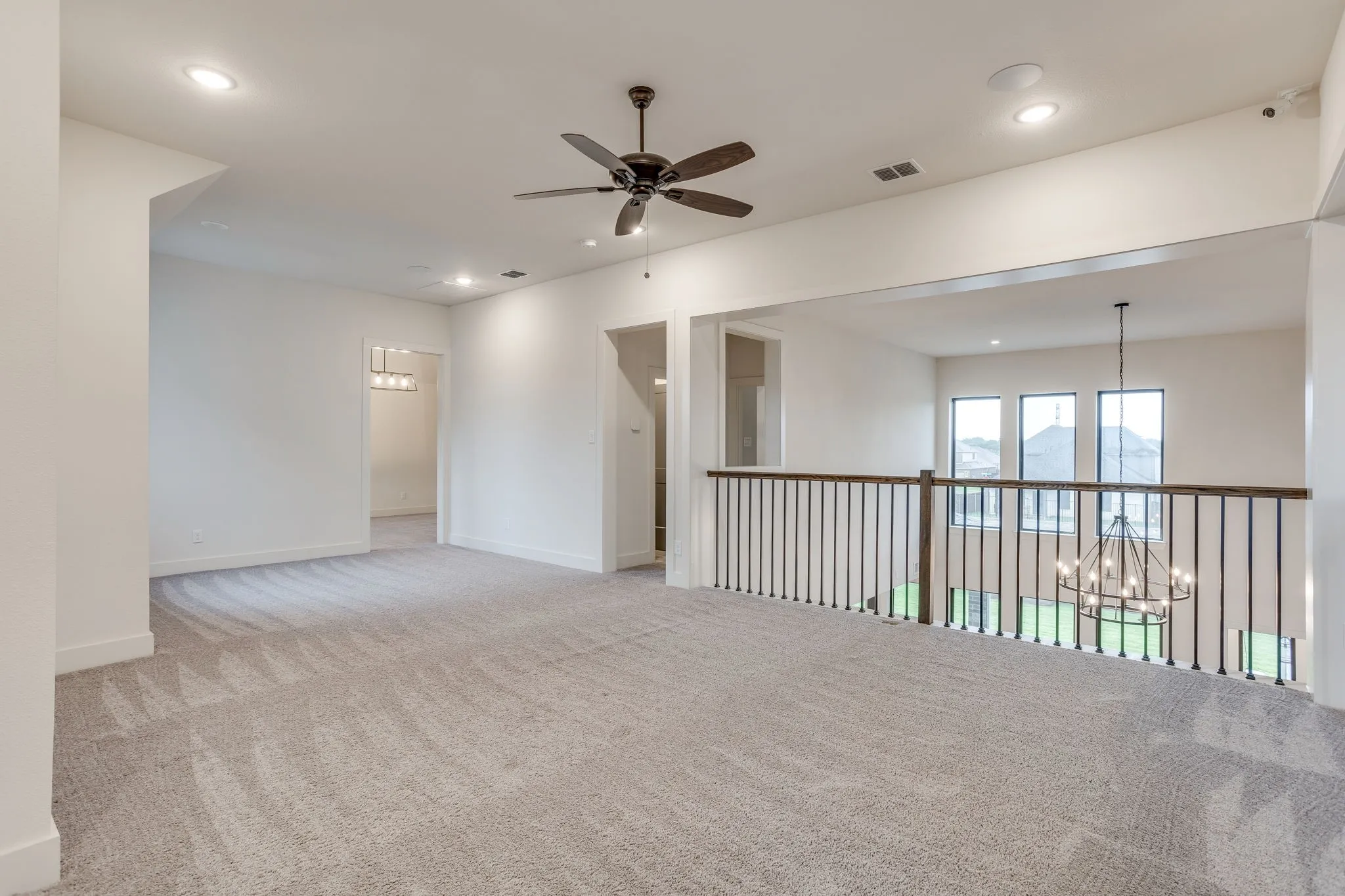 Spacious carpeted landing featuring recessed lighting, a ceiling fan, and an open railing overlooking a lower level with multiple windows