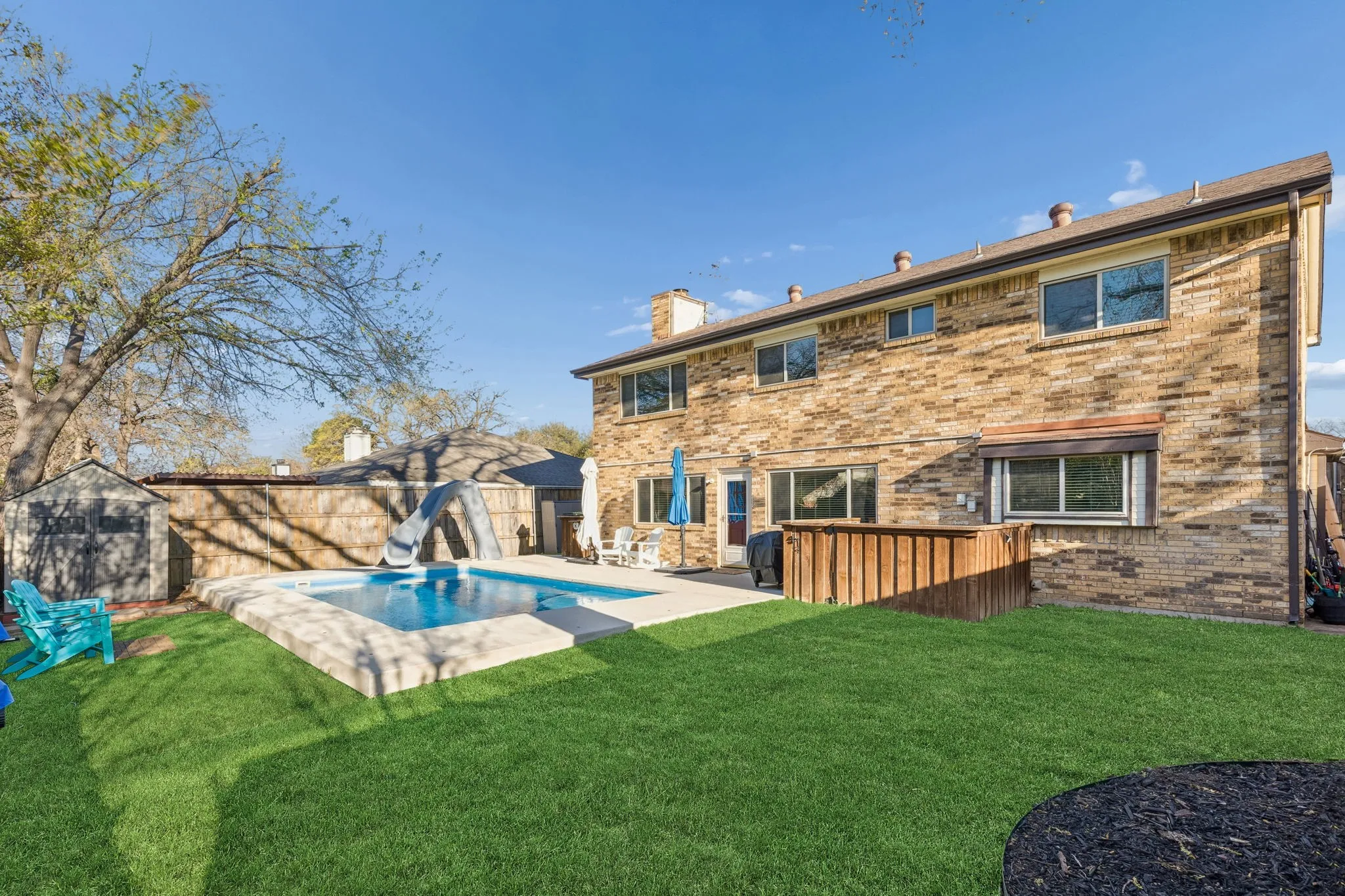Back of property with a storage unit, a chimney, brick siding, and a fenced backyard