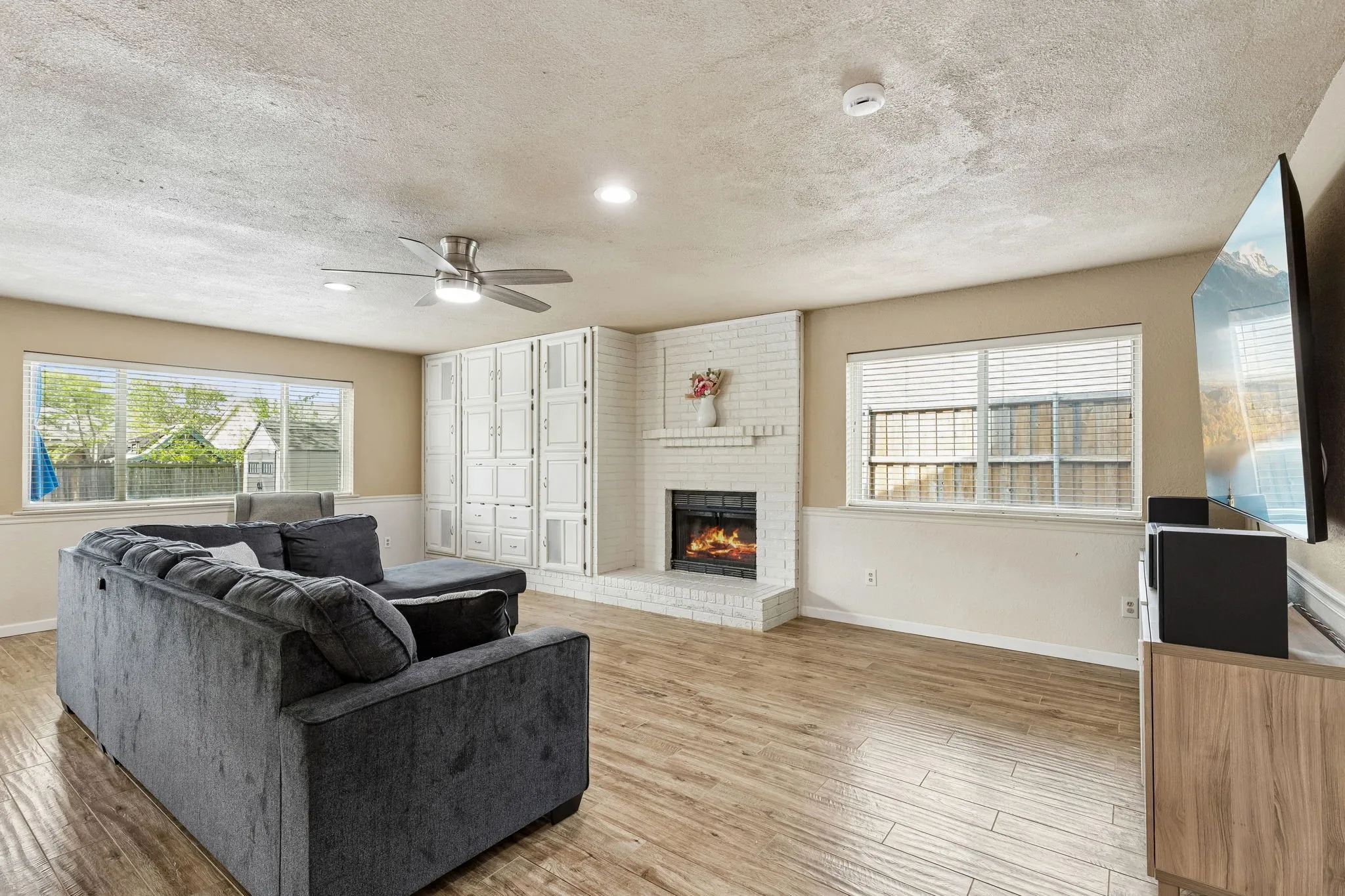 Living room with a ceiling fan, light wood-style floors, a textured ceiling, recessed lighting, and a brick fireplace
