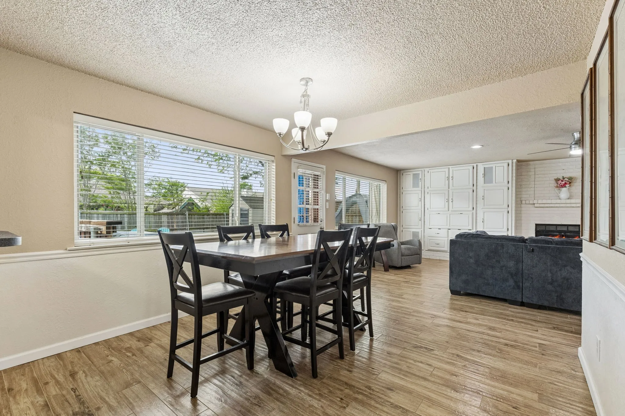 Dining space with a textured ceiling, light wood finished floors, a large fireplace, suspended lighting, and a ceiling fan