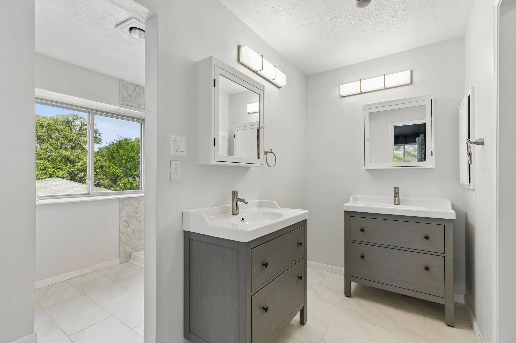 Bathroom with two vanities, light marble finish flooring, and a textured ceiling