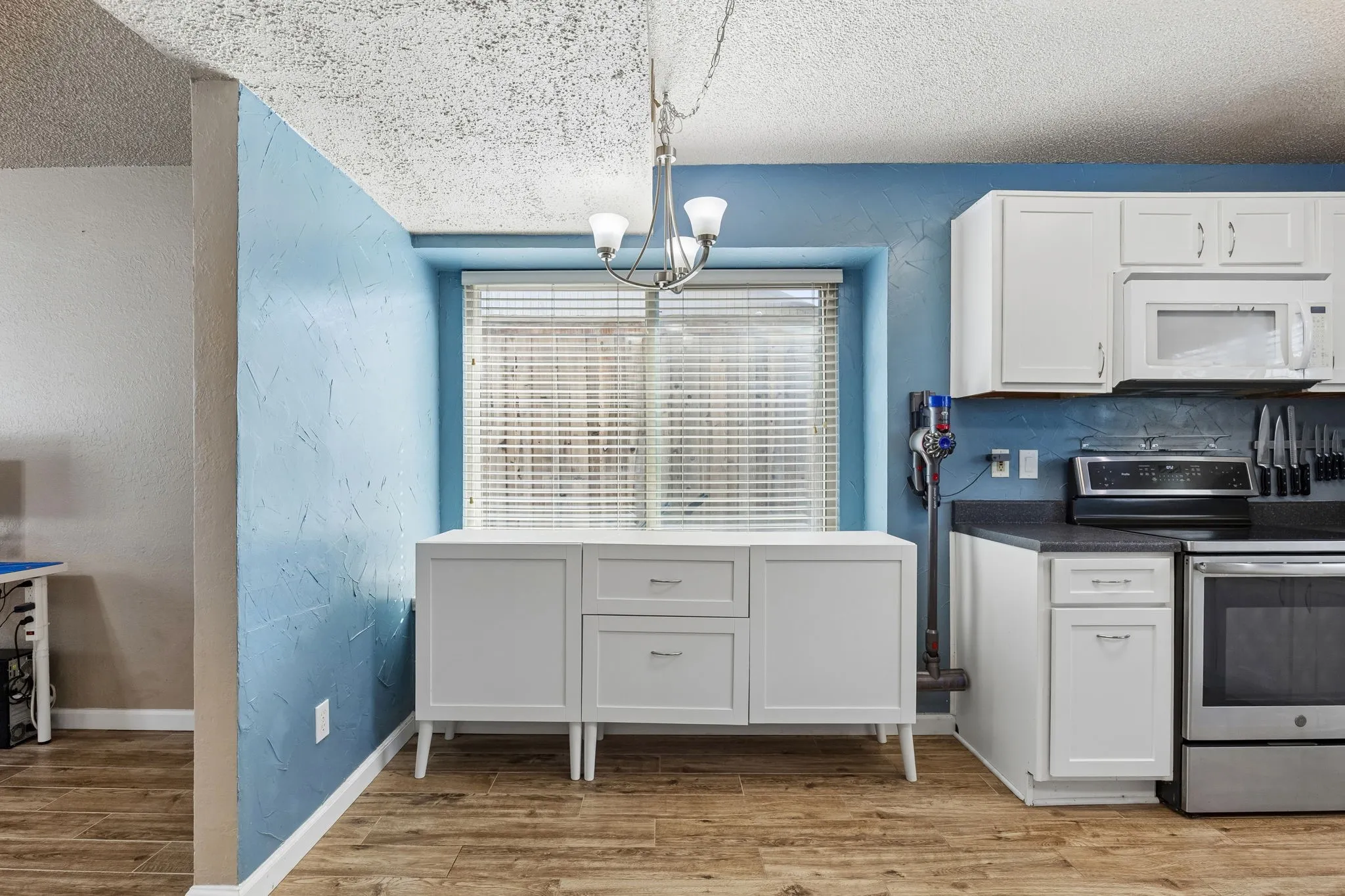 Kitchen with stainless steel electric stove, a textured wall, light wood finished floors, a textured ceiling, and dark countertops