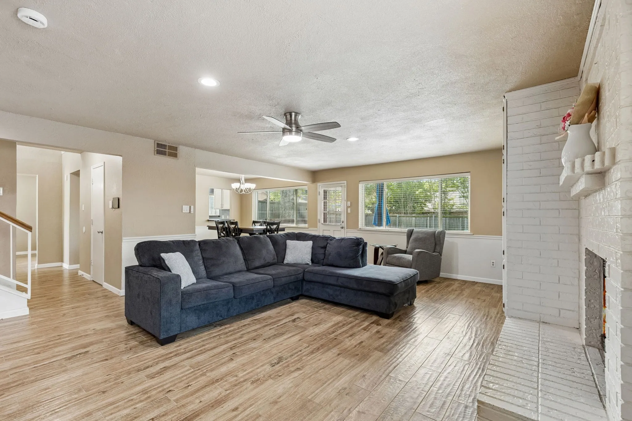 Living area featuring light wood-style flooring, a textured ceiling, a ceiling fan, and a brick fireplace