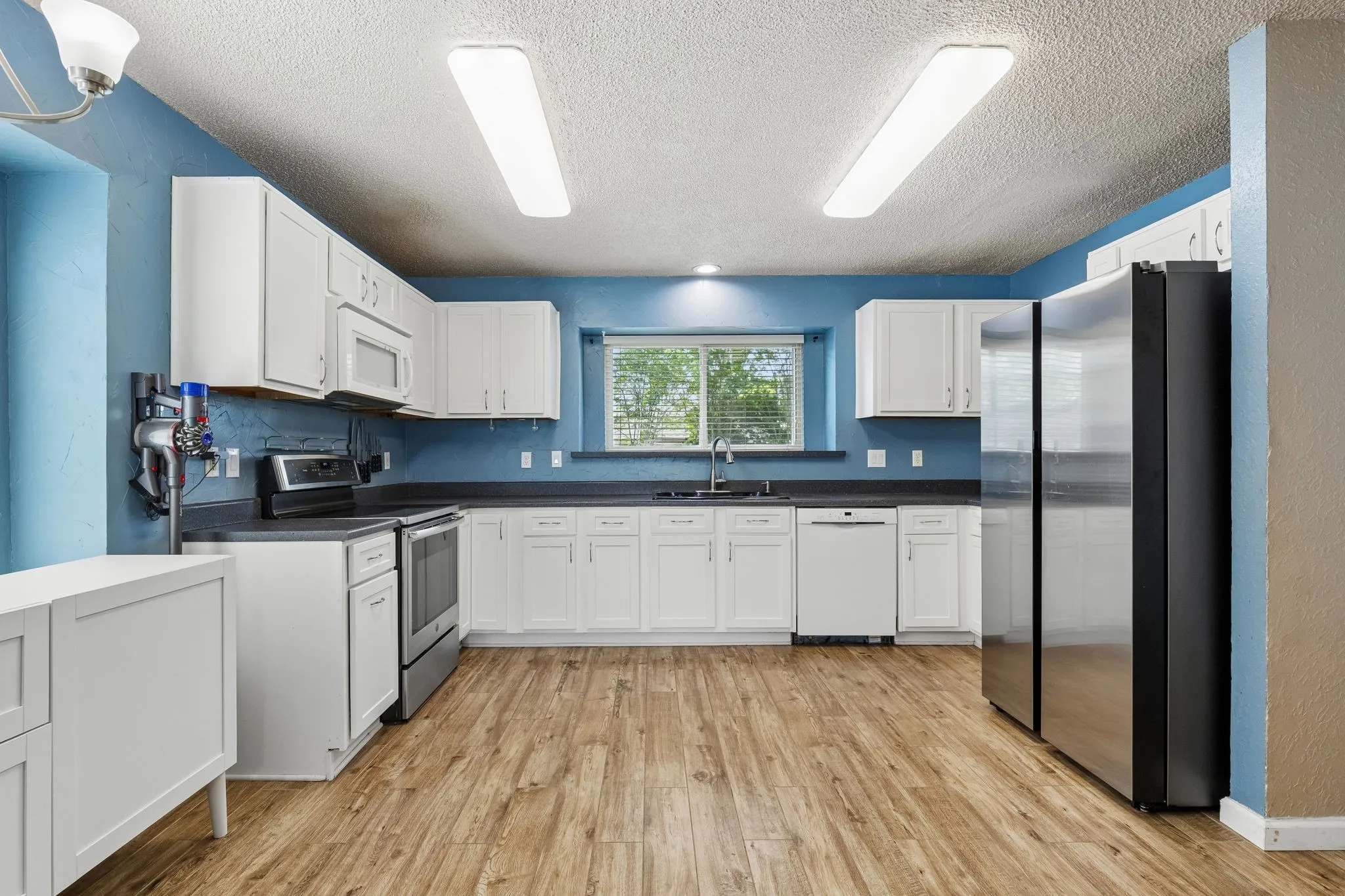 Kitchen featuring stainless steel appliances, dark countertops, white cabinets, light wood finished floors, and a textured ceiling